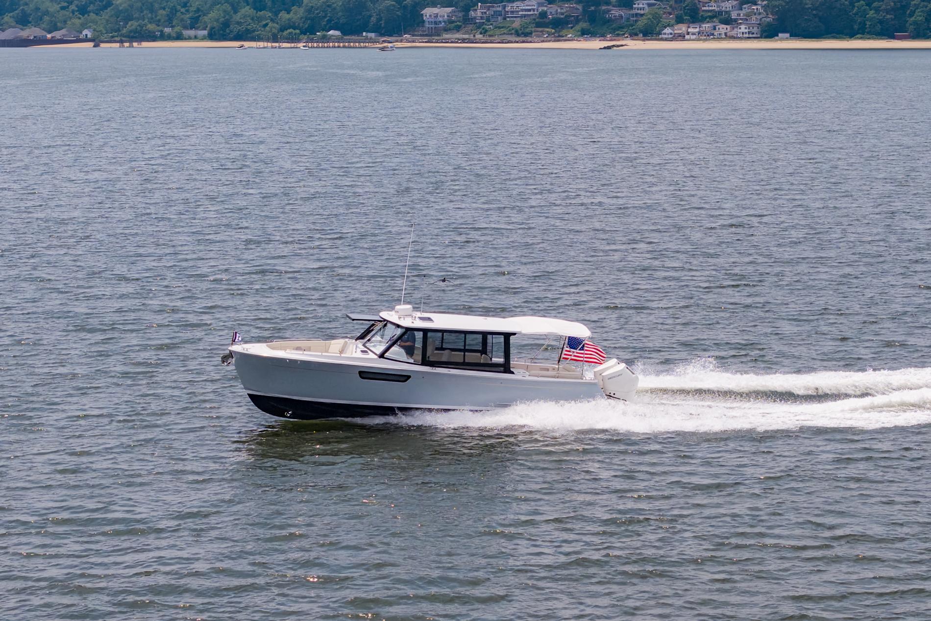 2025 MJM 3 boat cruising on water with American flag, scenic shoreline background.