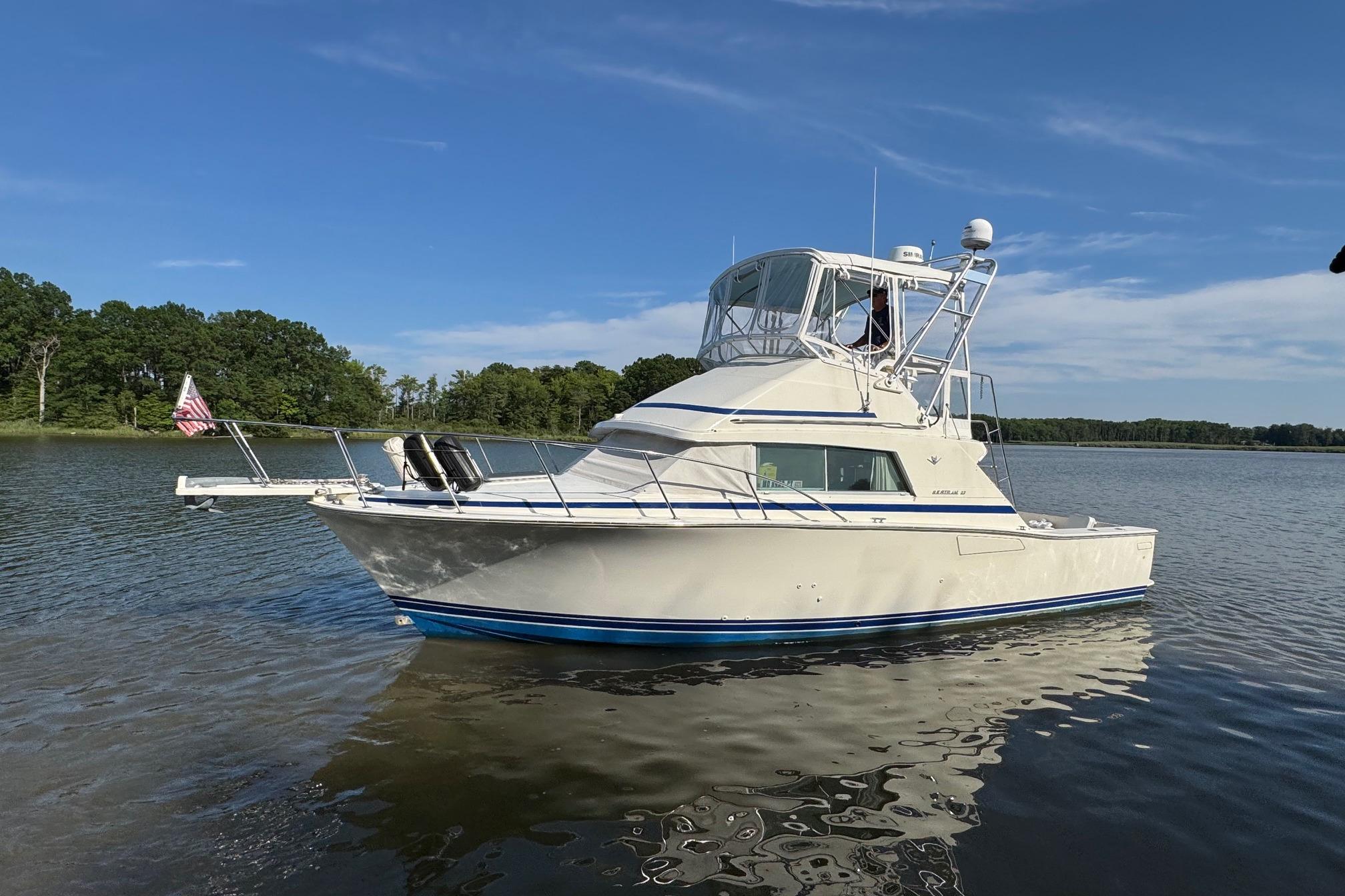 1987 Bertram 33 Sport Fisherman boat on calm water under clear blue sky.