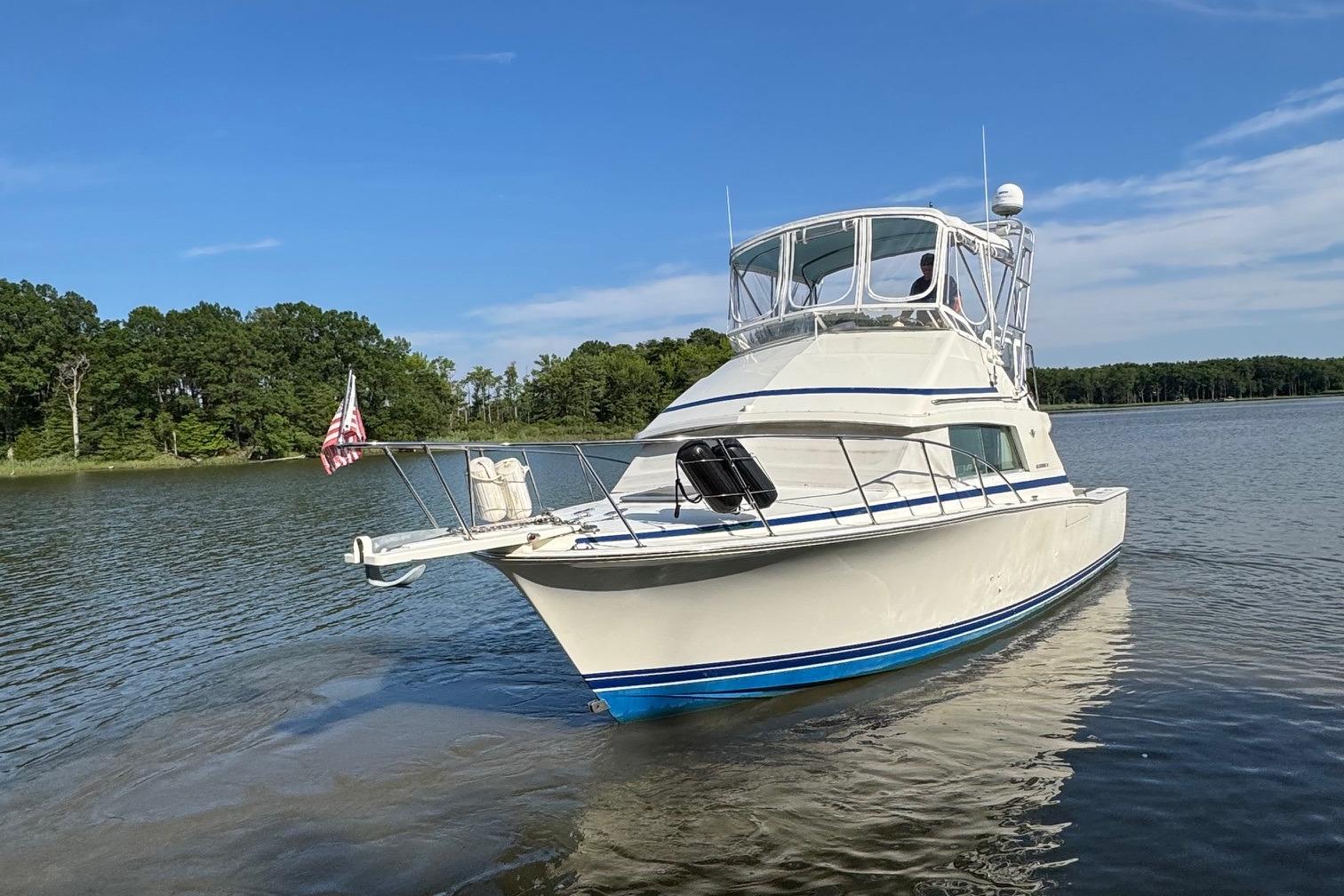 1987 Bertram 33 Sport Fisherman boat on calm water, clear sky background.