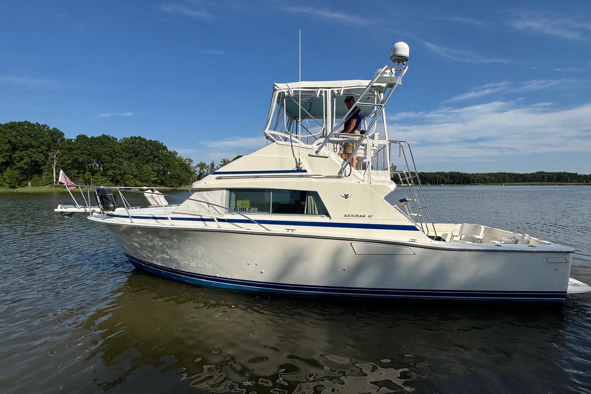 1987 Bertram 33 Sport Fisherman boat on calm water, clear sky background.