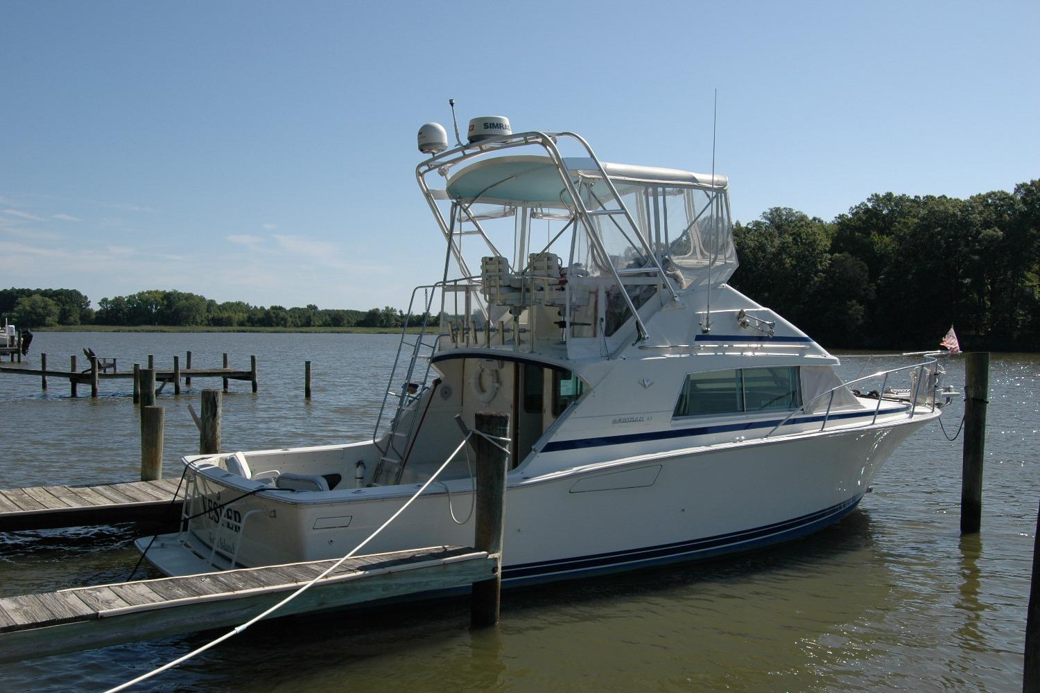 1987 Bertram 33 Sport Fisherman docked on a calm lake under clear skies.