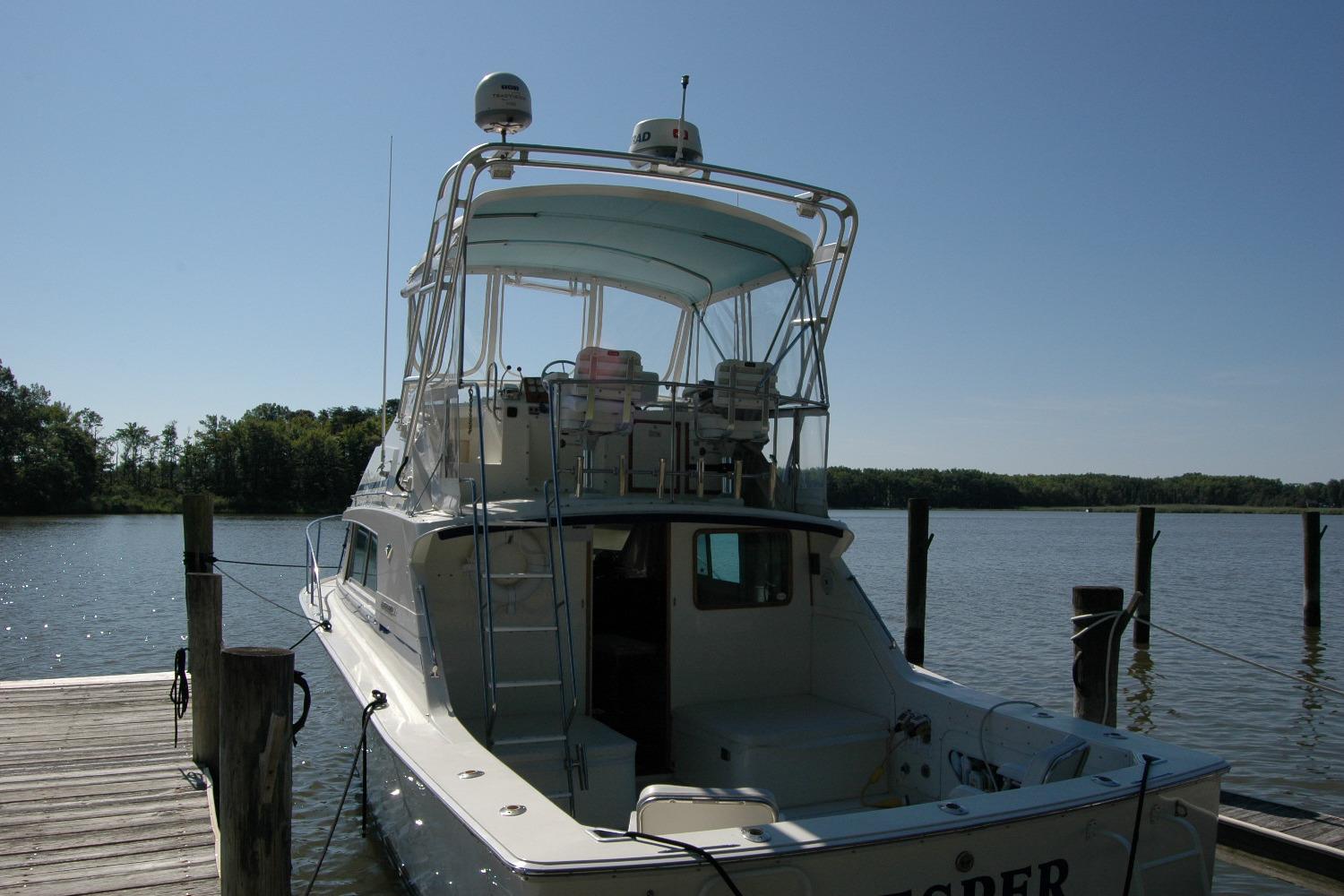 1987 Bertram 33 Sport Fisherman docked by a serene lake under clear skies.