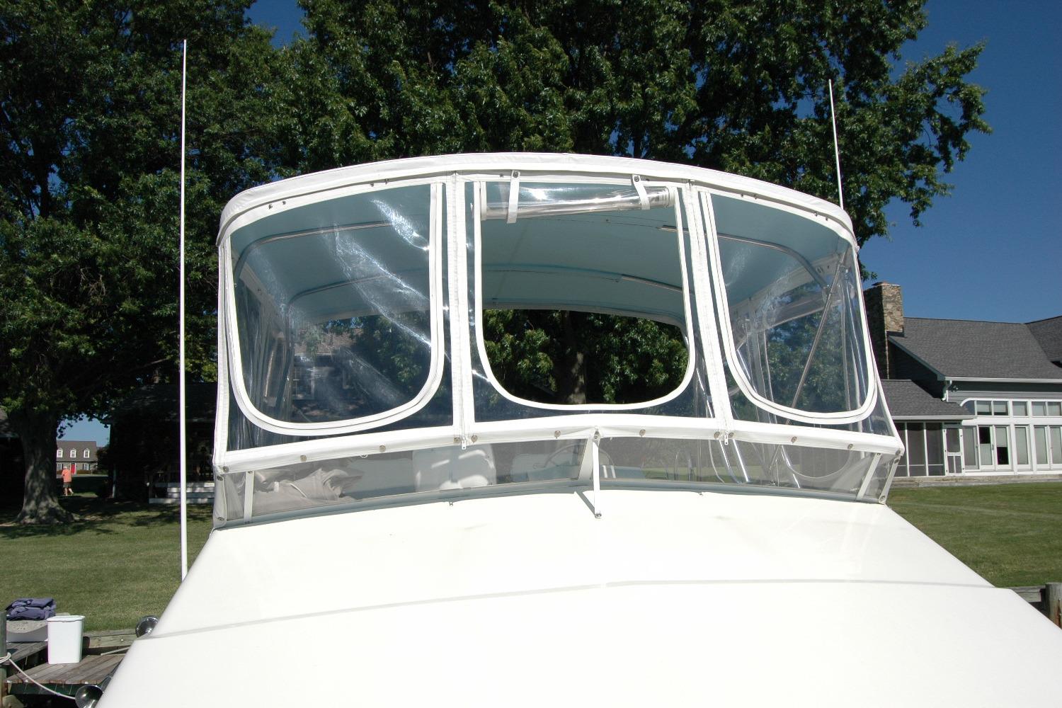 1987 Bertram 33 Sport Fisherman boat with clear enclosure, docked near trees and buildings.