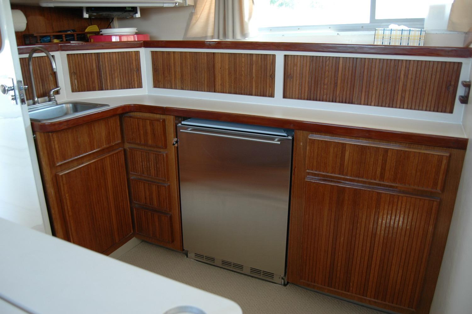1987 Bertram 33 Sport Fisherman galley with wood cabinetry and stainless steel fridge.
