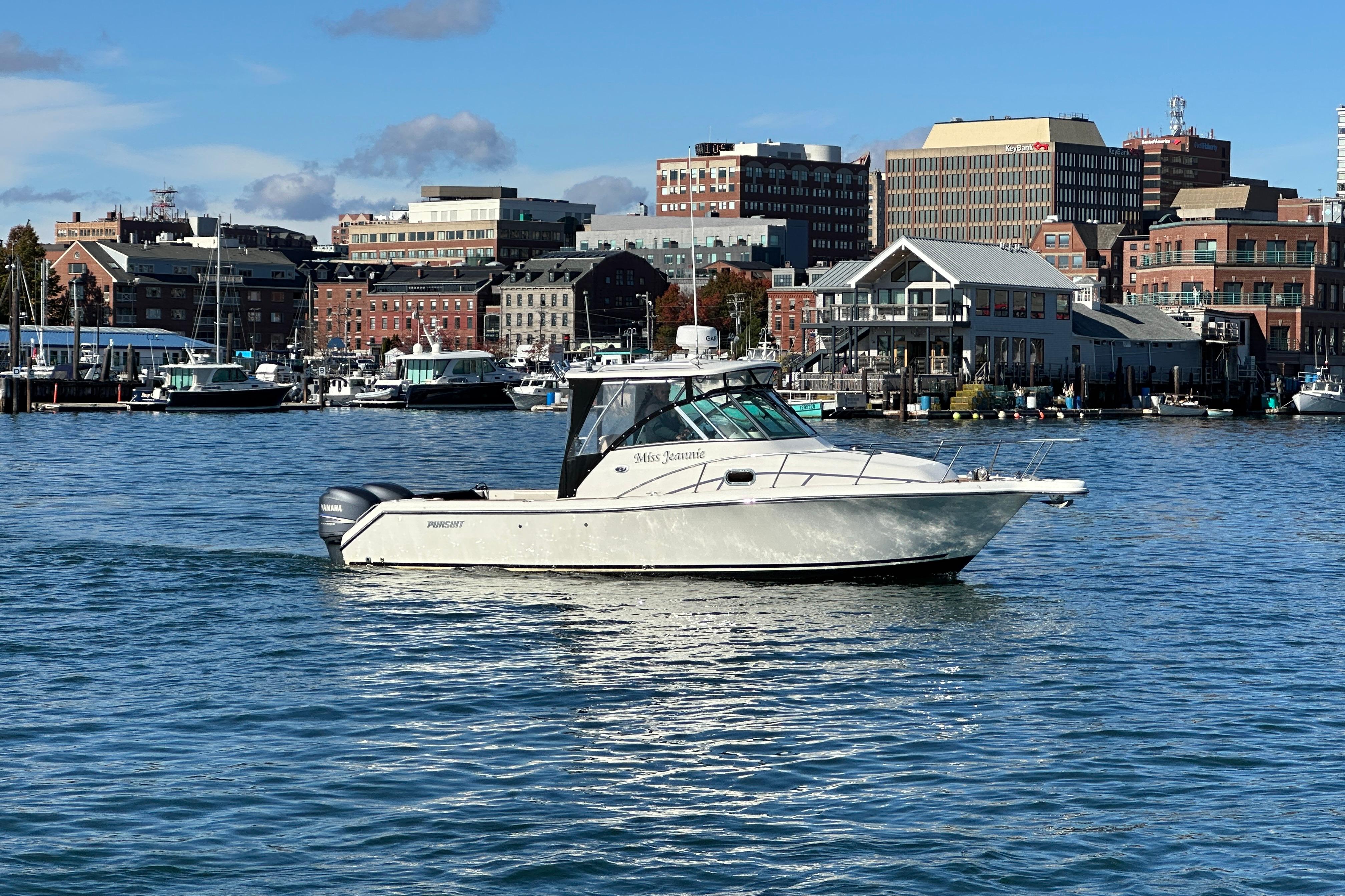 2007 Pursuit OS 285 Offshore boat cruising in a scenic harbor with city skyline.