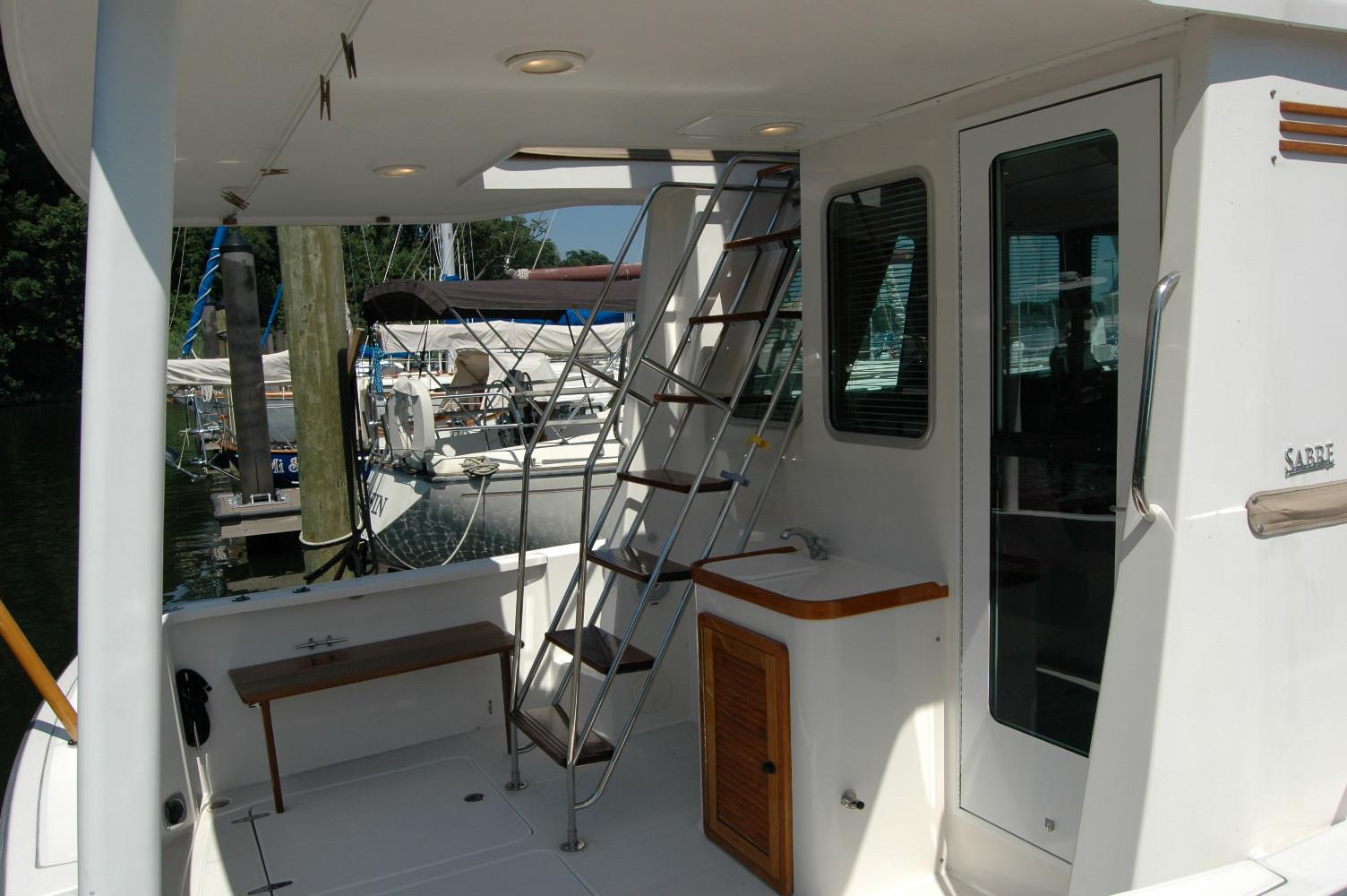 2006 Sabre 36 Flybridge Sedan yacht with ladder, bench, and docked boats in background.