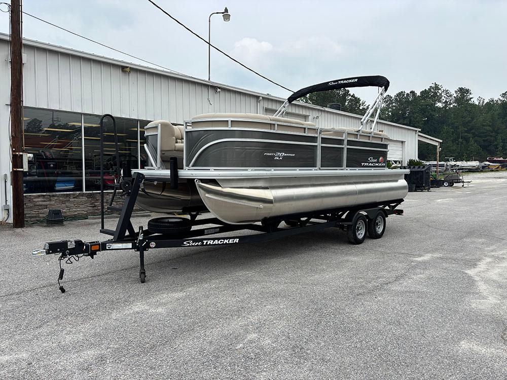 2025 Sun Tracker Party Barge 20 DLX pontoon boat on trailer, parked outside a building.