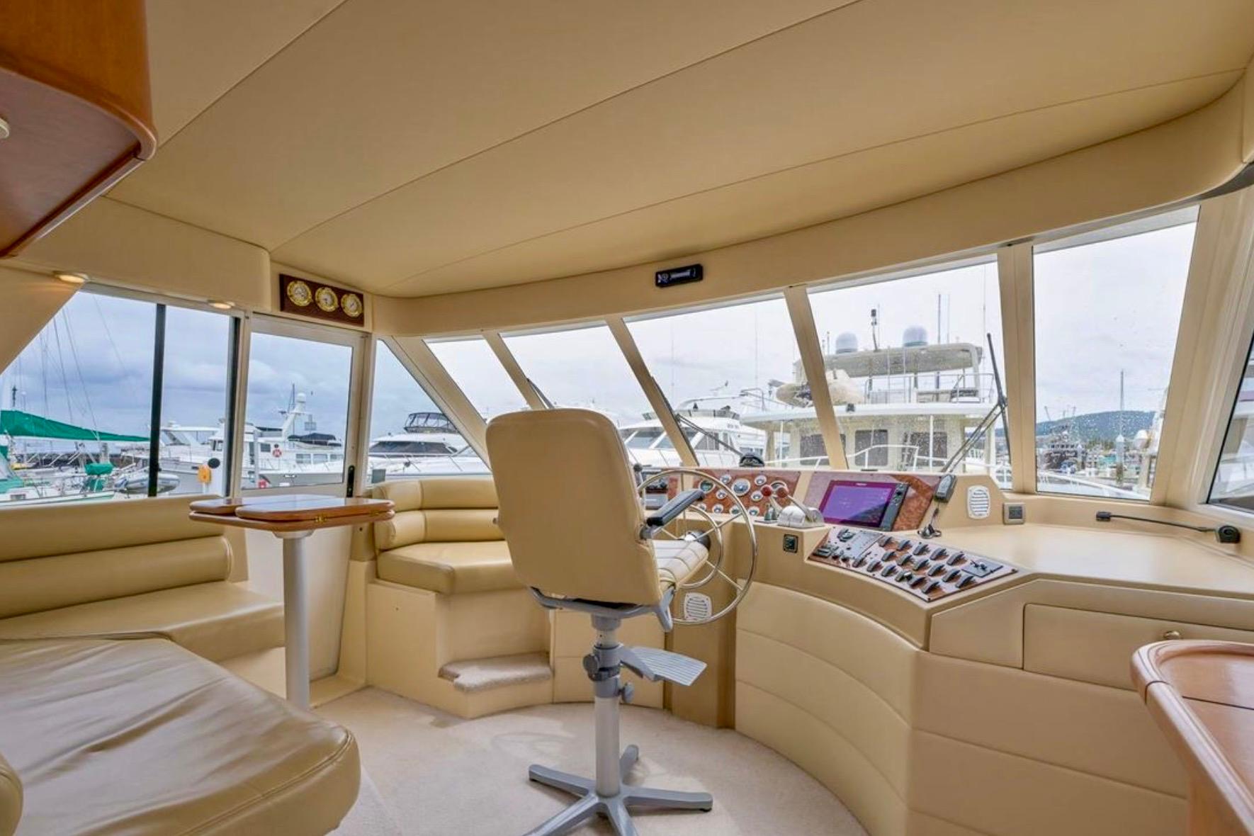 Luxurious 2004 Meridian 490 Pilothouse interior with helm, beige seating, and marina view.