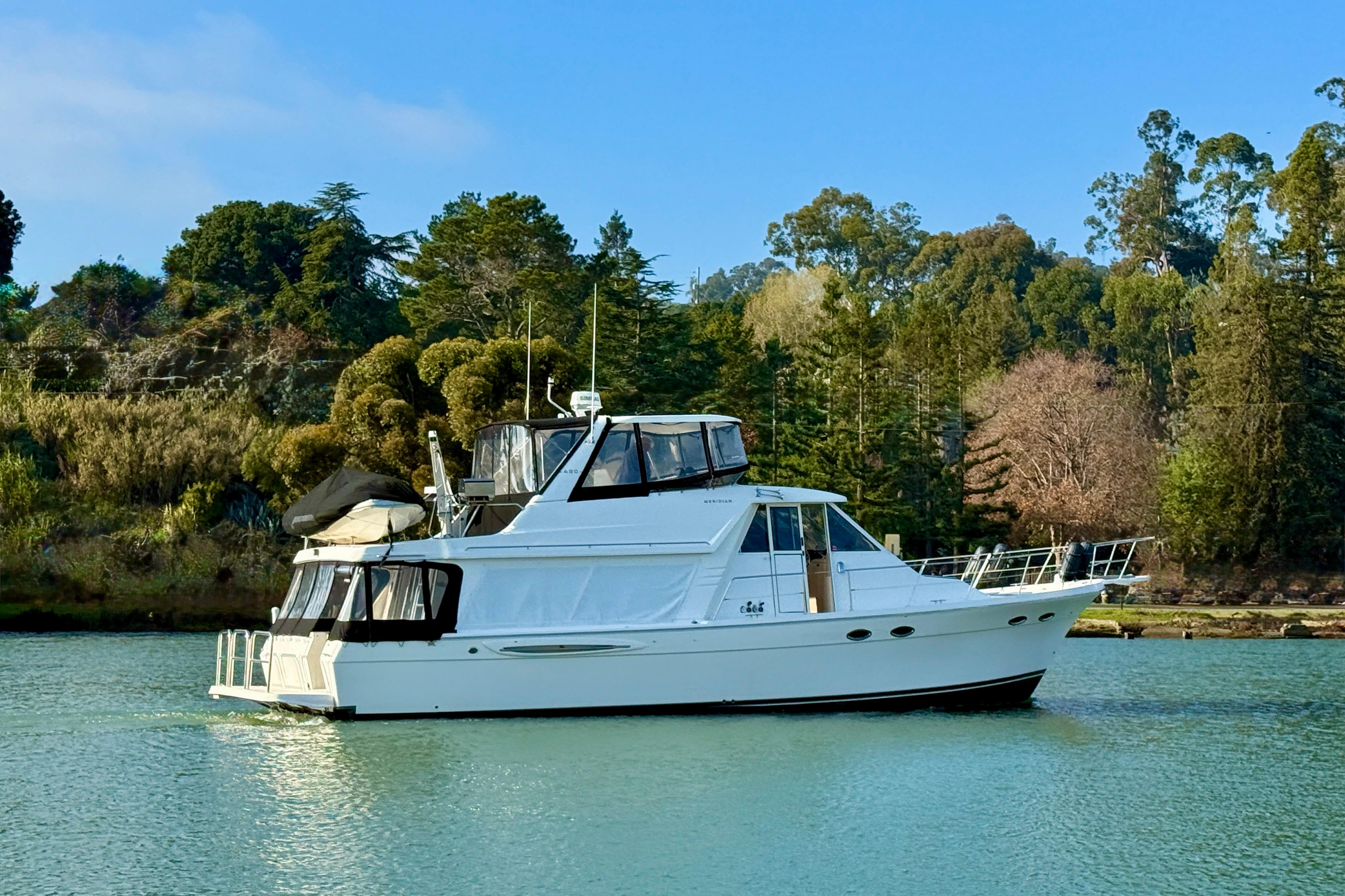 2004 Meridian 490 Pilothouse on calm water with wooded backdrop.