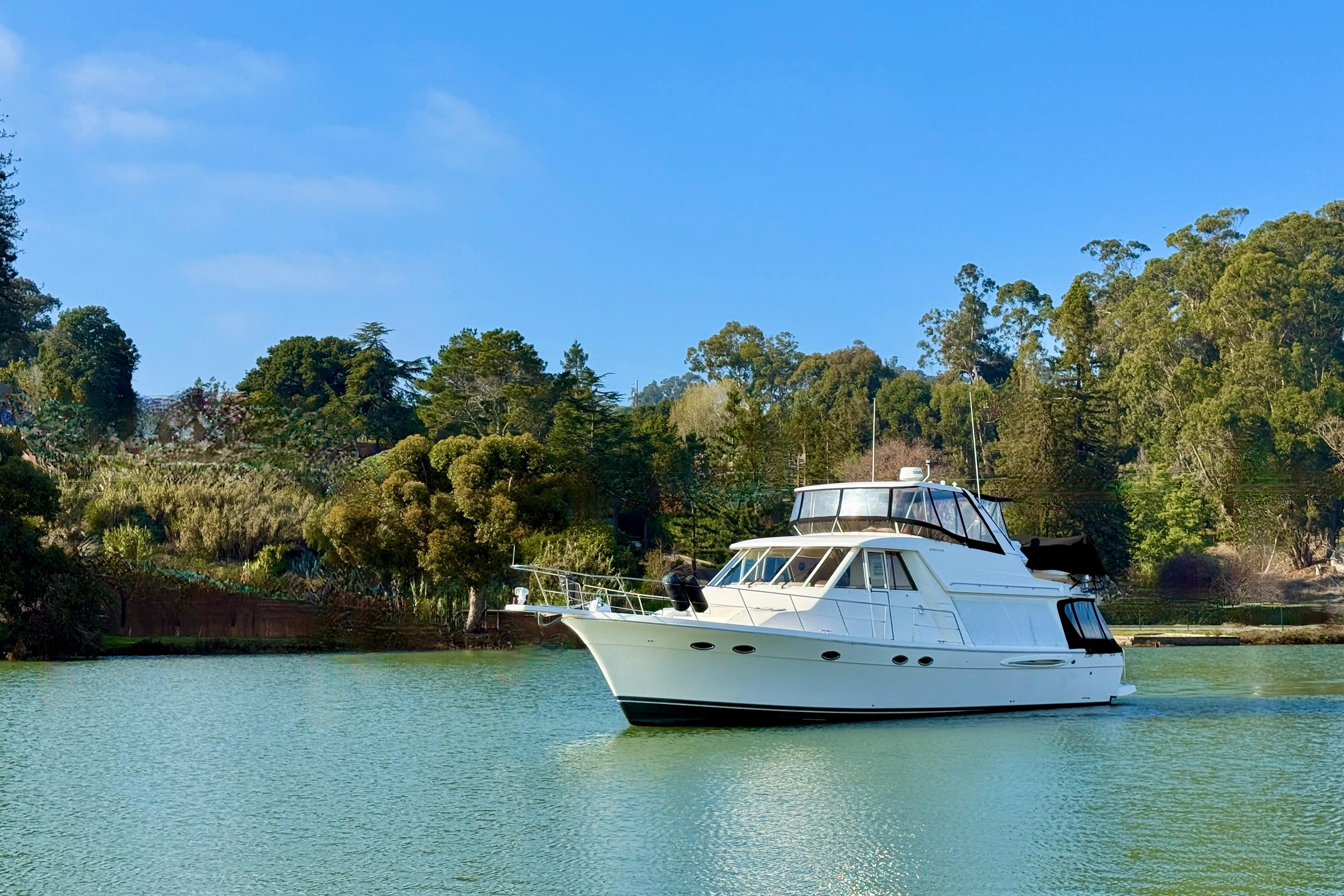 2004 Meridian 490 Pilothouse yacht cruising on a serene lake with lush greenery.