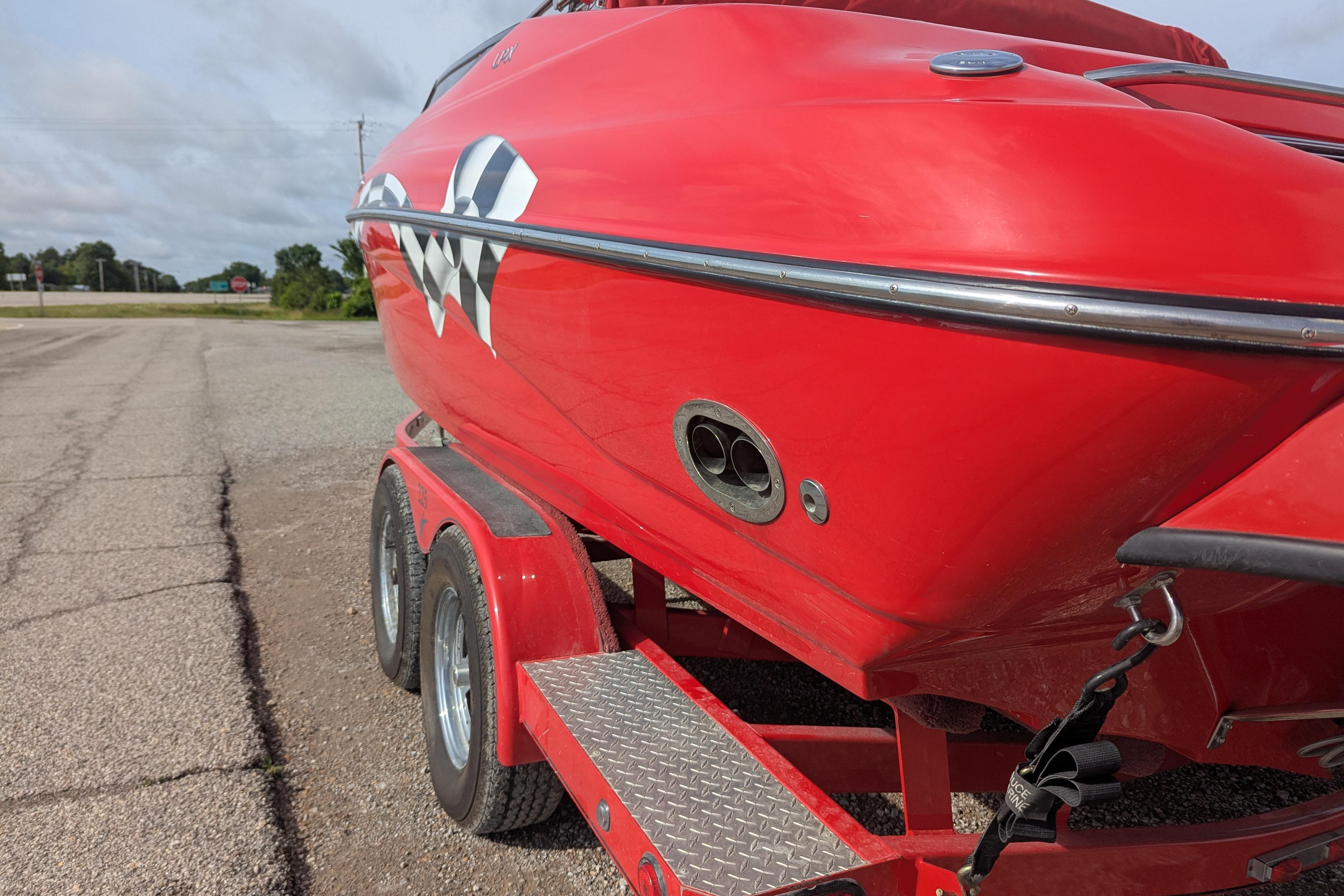 Red 2004 Crownline 225 BR boat on trailer, checkered flag design, parked on roadside.