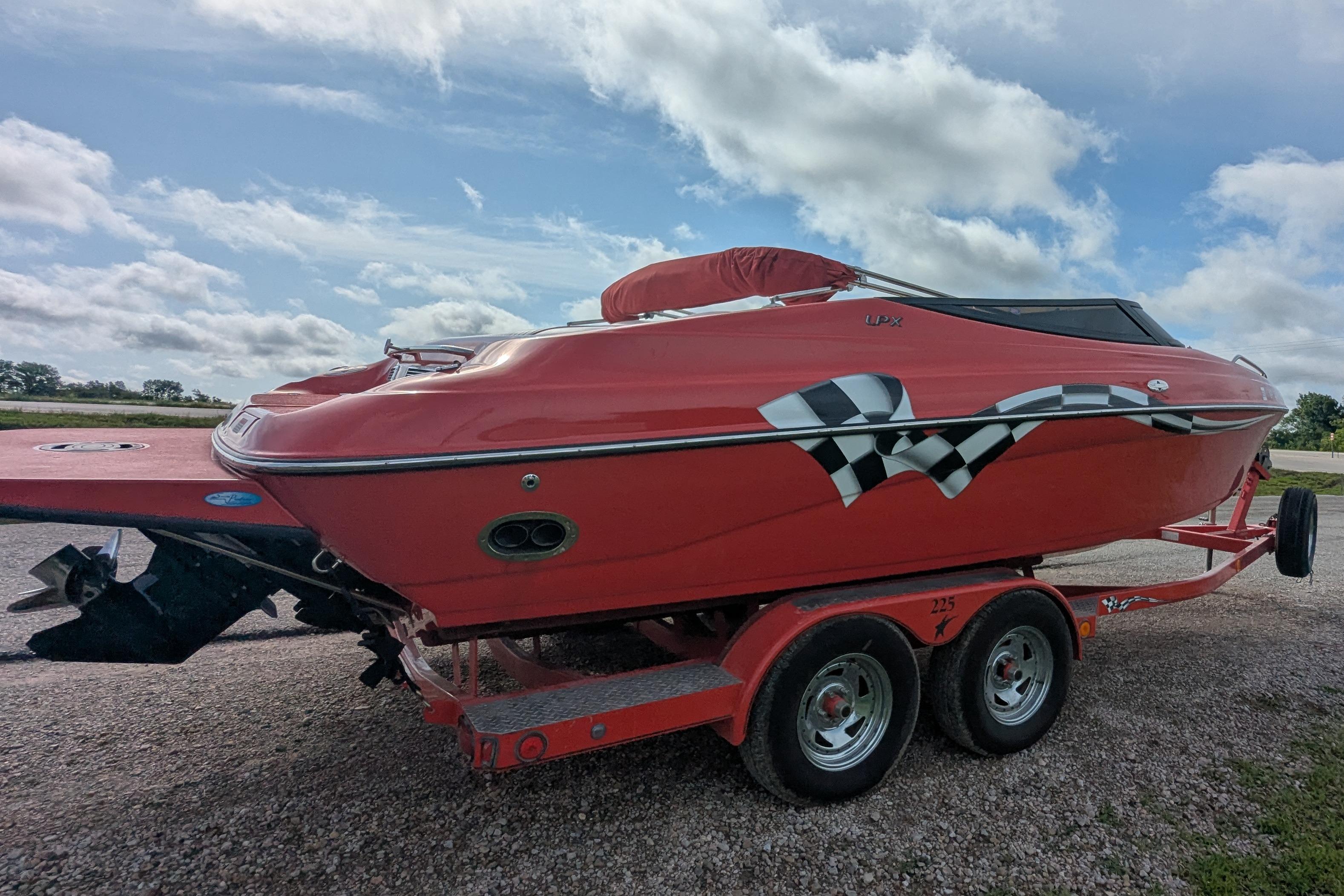 2004 Crownline 225 BR boat on trailer, red with checkered flag design, parked outdoors.