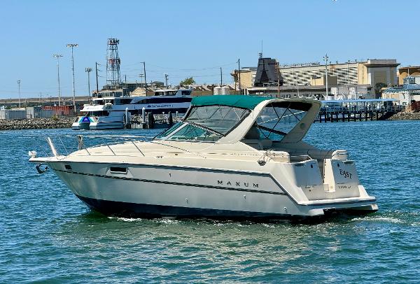 1997 Maxum 3200 SCR boat cruising in a harbor with industrial background.