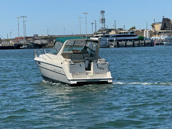1997 Maxum 3200 SCR boat cruising in a harbor with cityscape background.