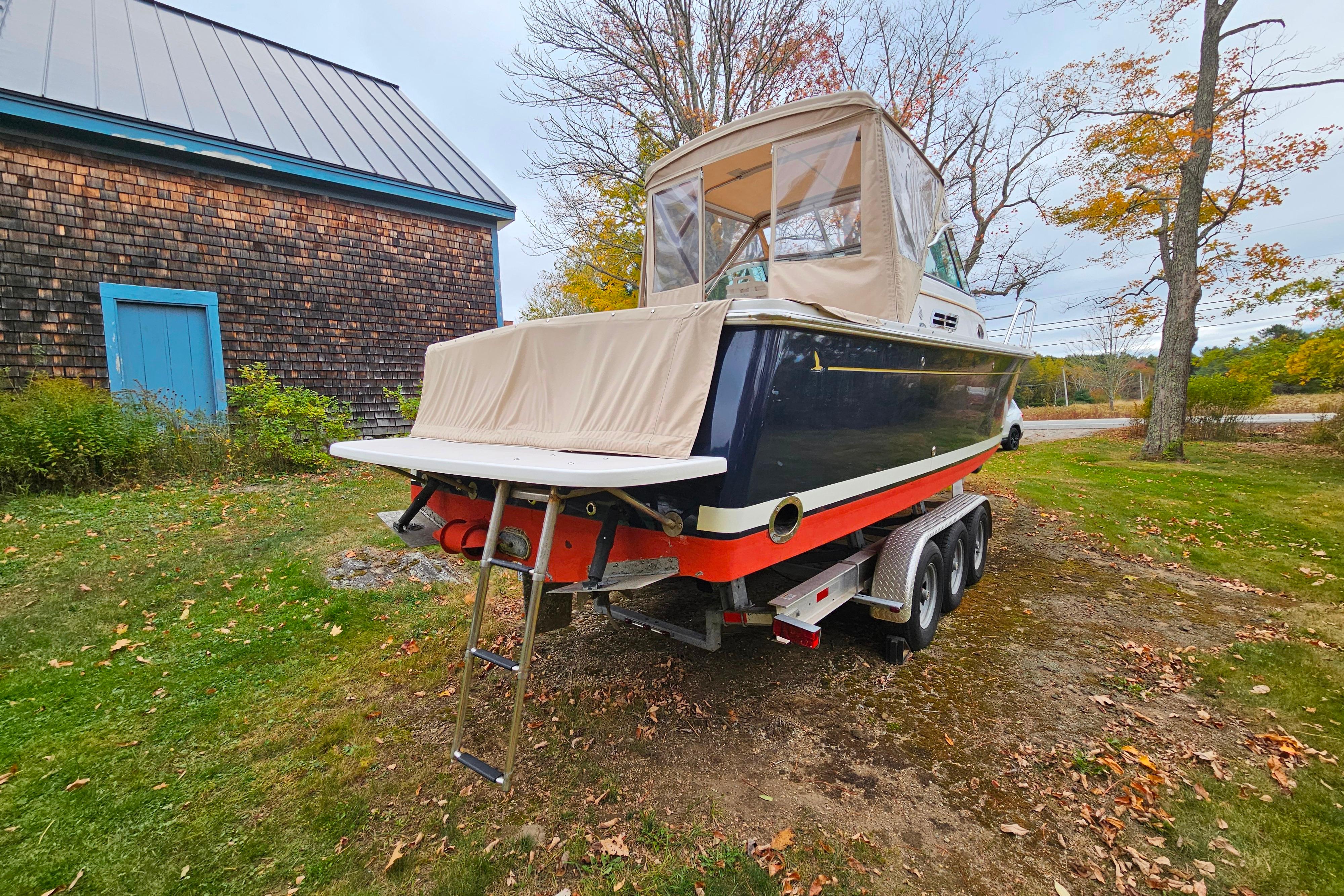 2006 Back Cove 26 boat on trailer, parked on grassy area near wooden building.