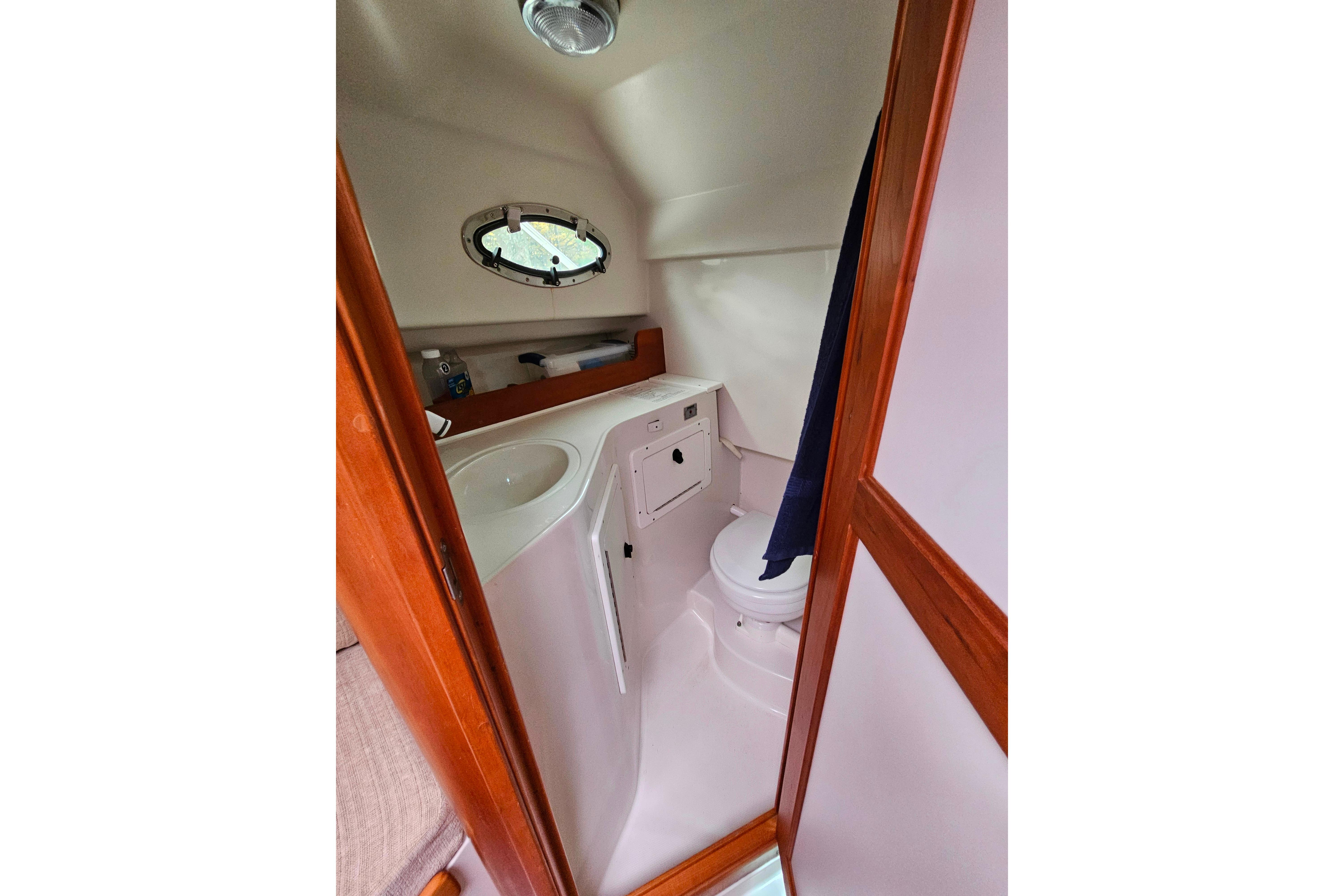 Compact bathroom in 2006 Back Cove 26 boat, featuring sink, toilet, and porthole window.