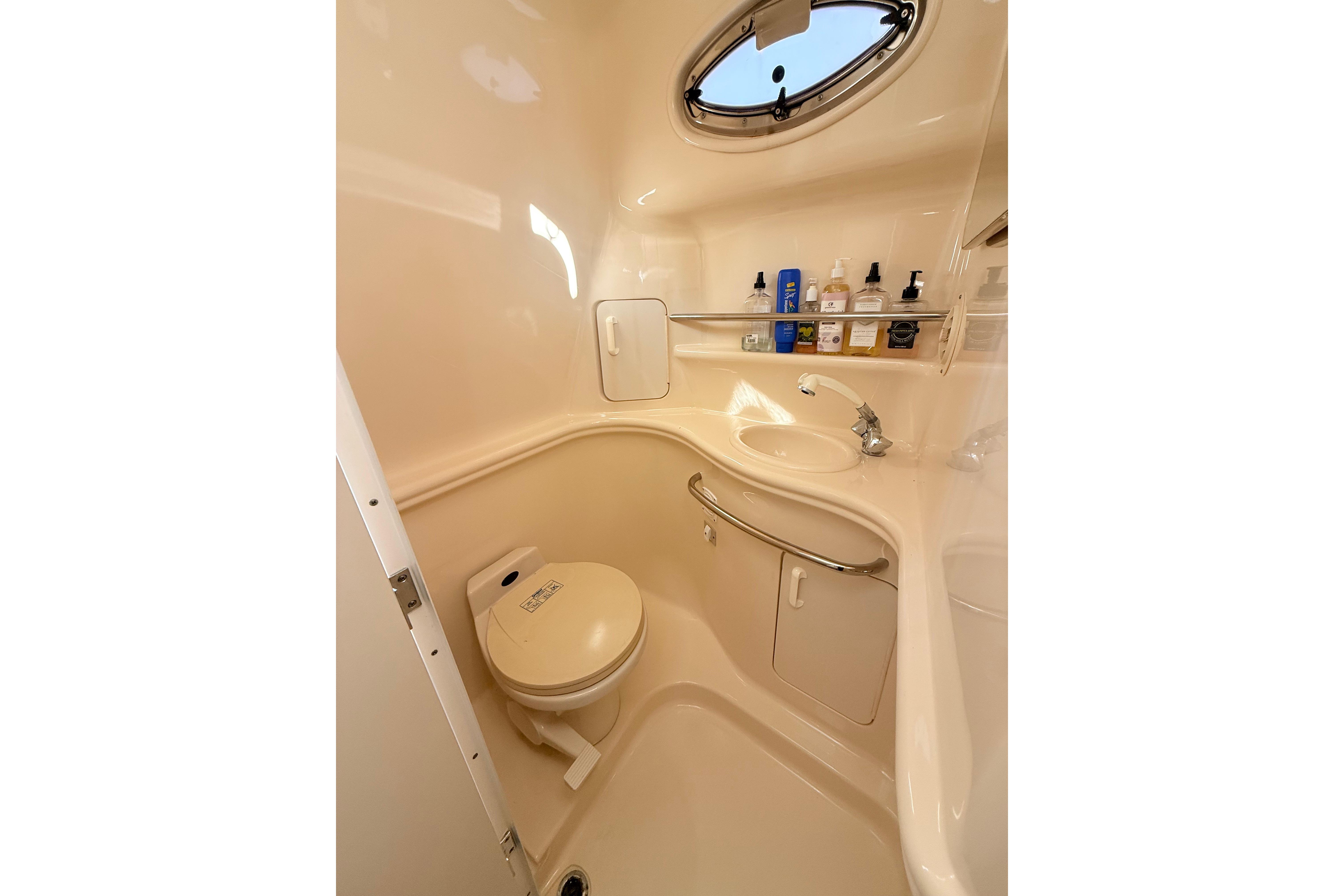 2001 Sea Ray 340 Sundancer bathroom with toilet, sink, and toiletries under a porthole window.