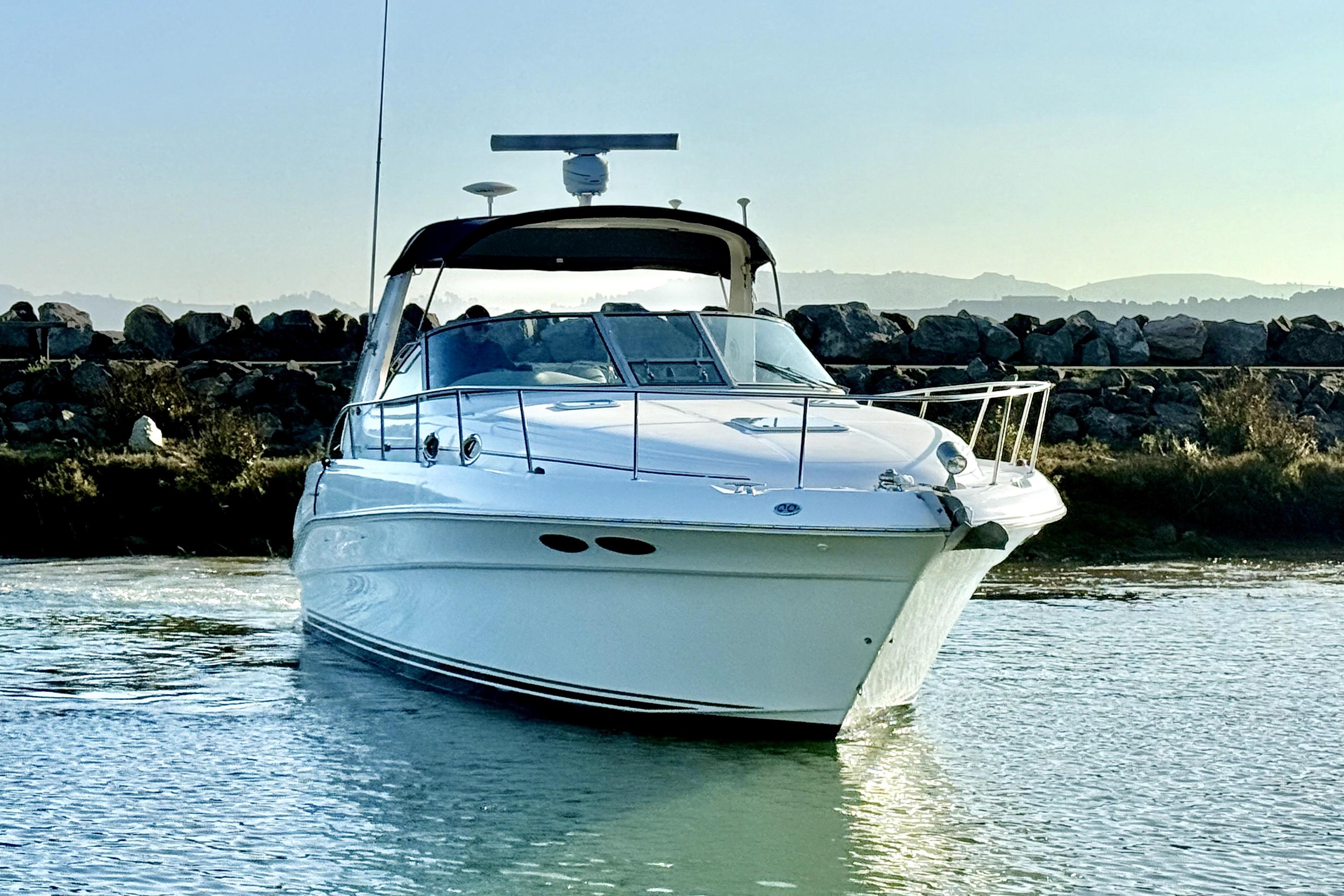 2001 Sea Ray 340 Sundancer yacht cruising on calm waters near rocky shoreline.