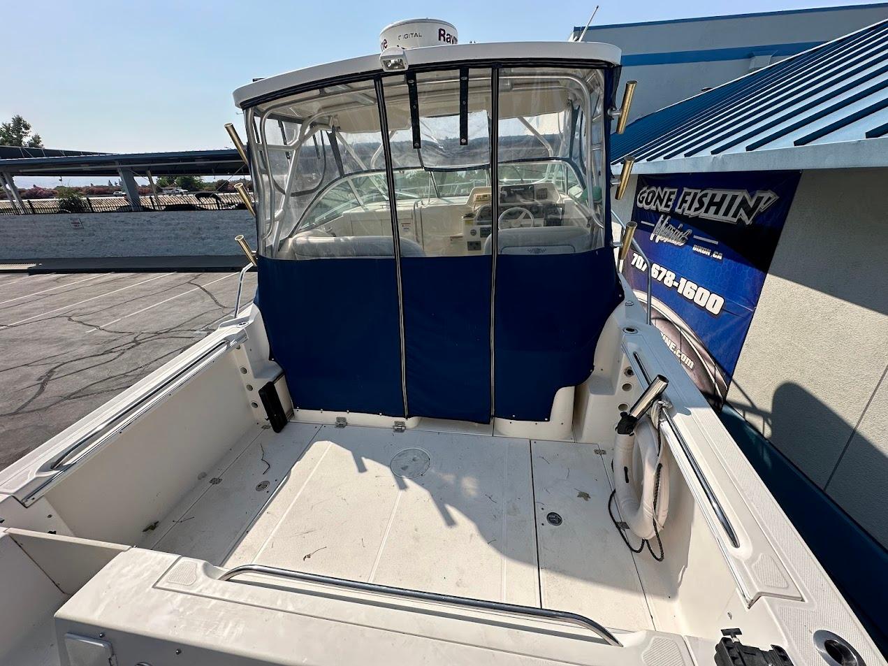 2006 Wellcraft 290 Coastal boat with blue canopy, docked near a fishing shop.