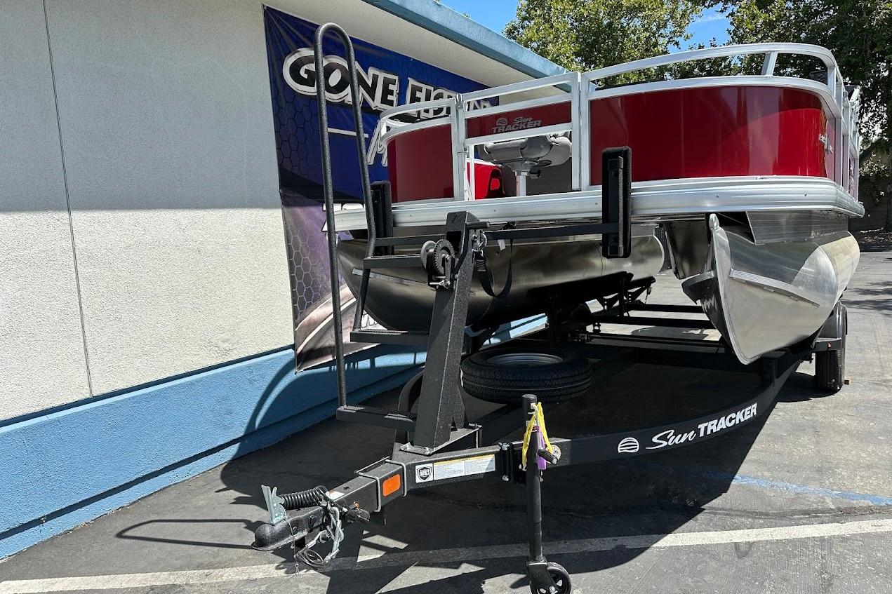 2026 Sun Tracker Bass Buggy 16 XL Select pontoon boat on trailer, parked outdoors.