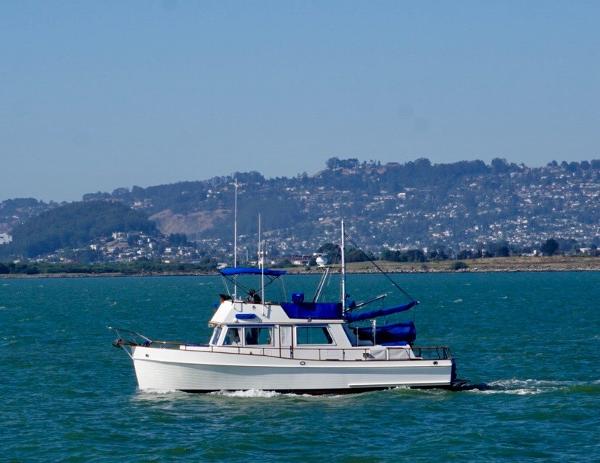 1982 Grand Banks Classic boat cruising on a scenic lake with hills in the background.