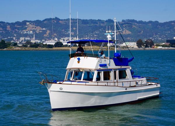 1982 Grand Banks Classic boat cruising on a scenic lake with hills in the background.