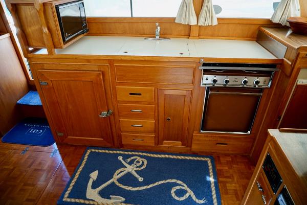 1982 Grand Banks Classic yacht kitchen with wooden cabinetry, stove, and nautical-themed rug.