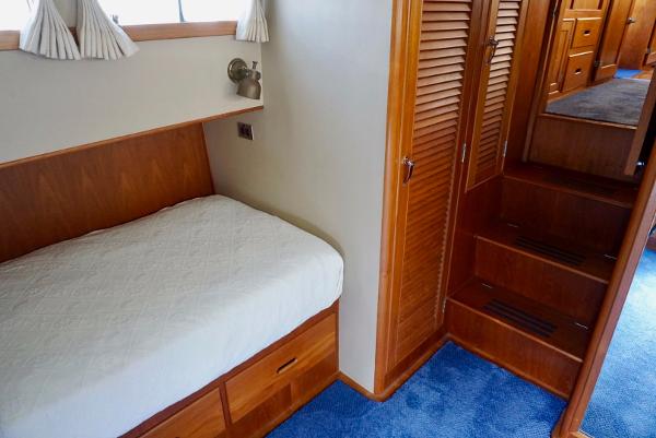 1982 Grand Banks Classic interior with wooden cabinetry, cozy bed, and blue carpeted flooring.