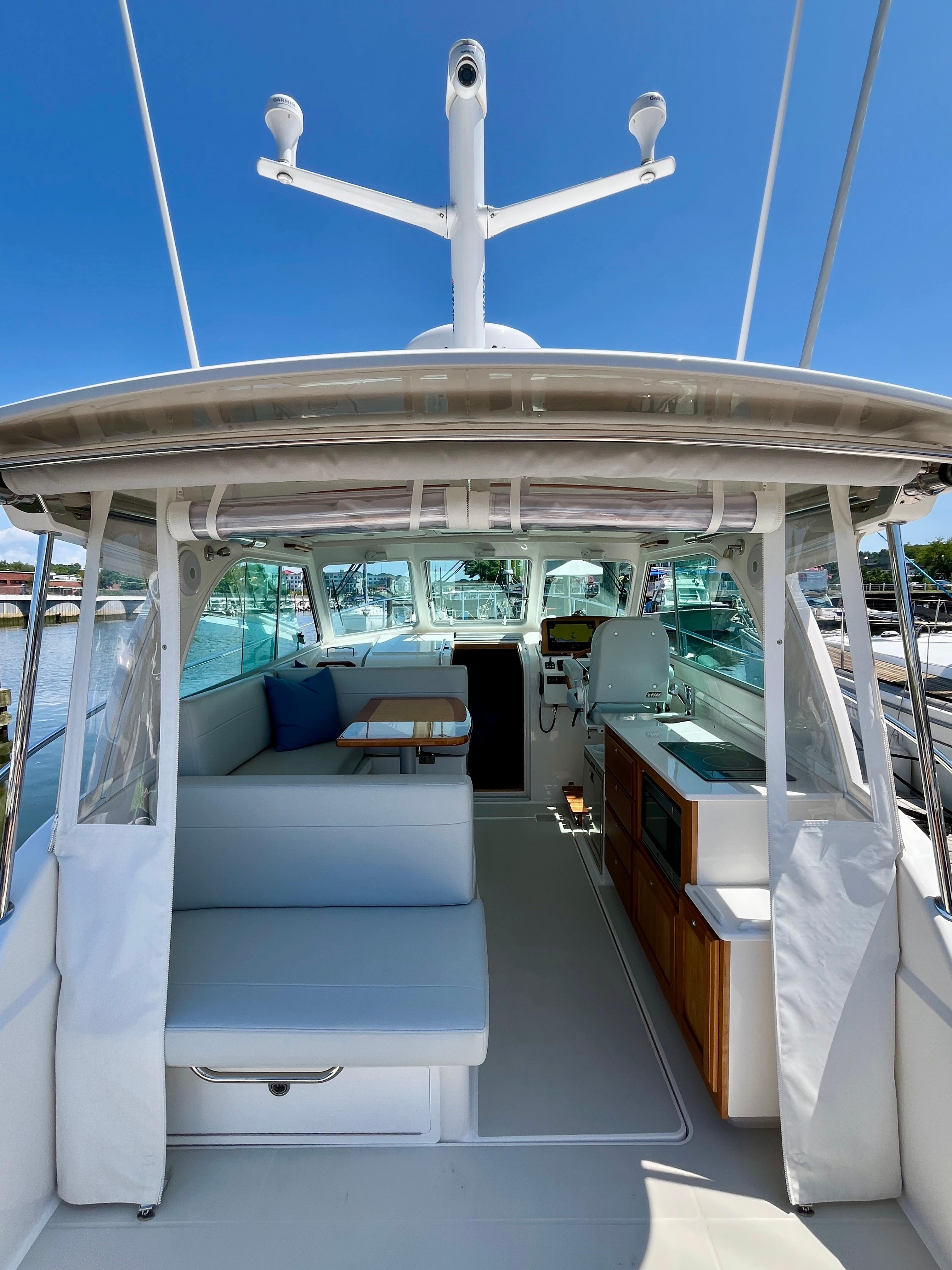 2023 Back Cove 34O yacht interior with seating, table, and helm under clear blue sky.