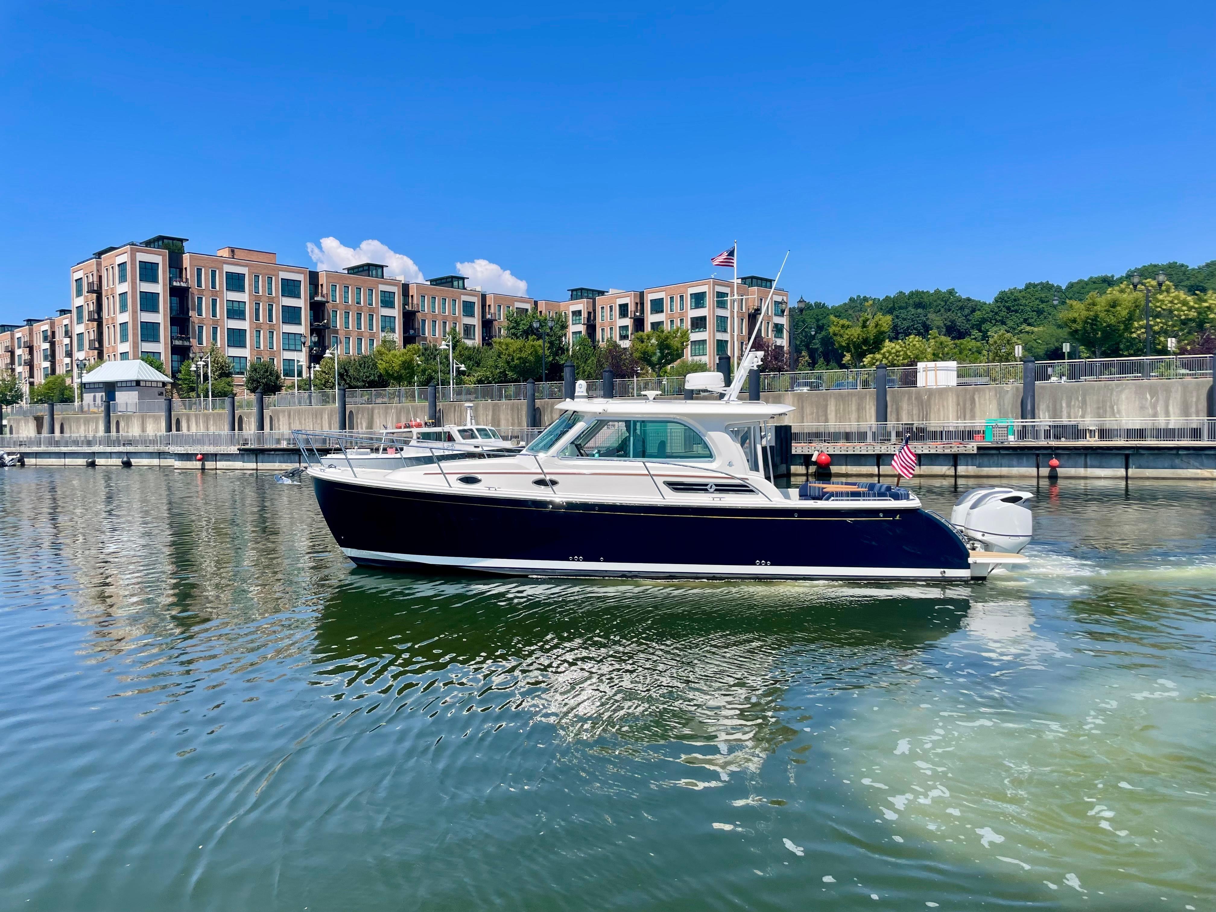 2023 Back Cove 34O boat cruising in a marina with modern buildings in the background.