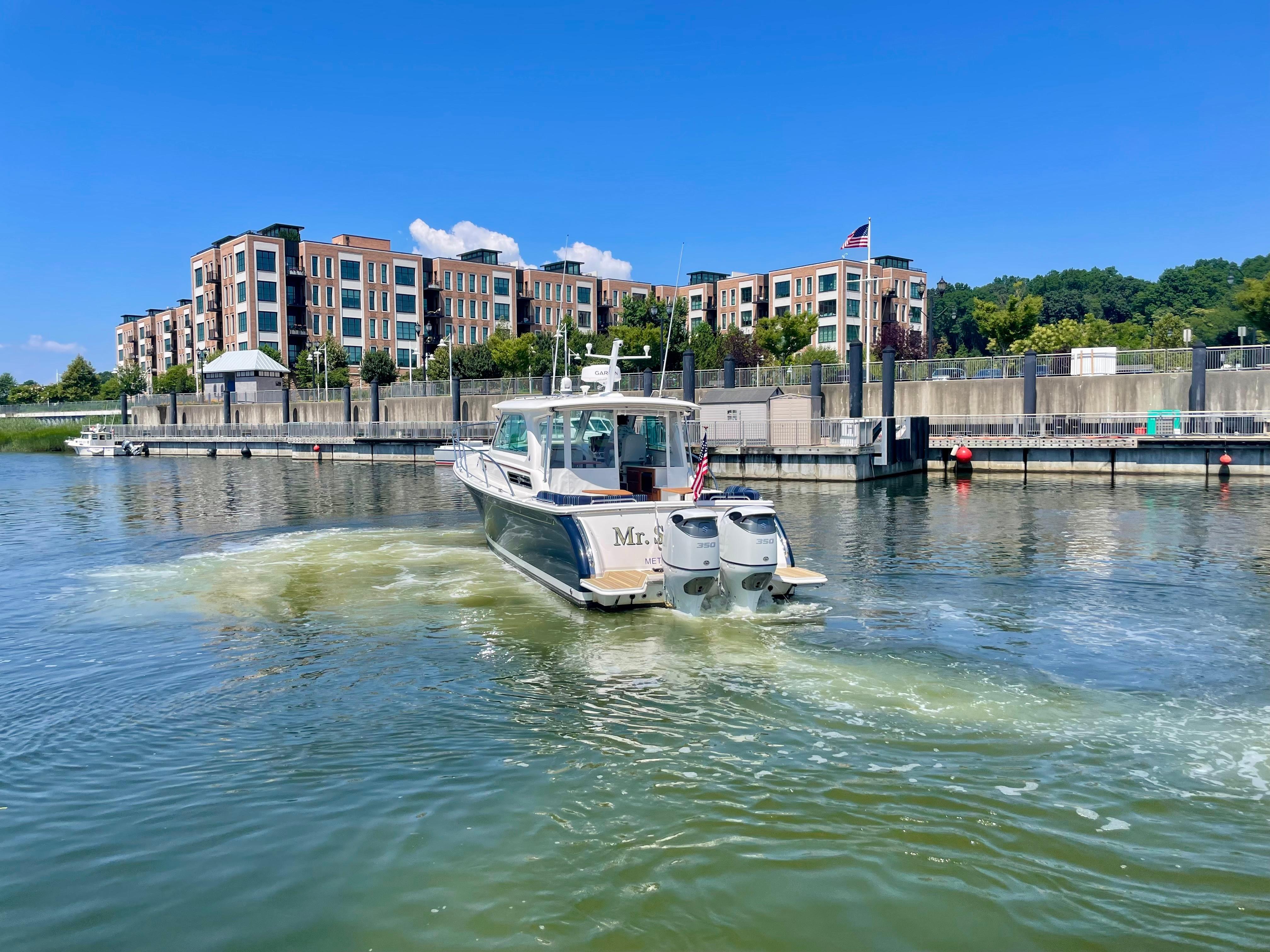 2023 Back Cove 34O boat cruising near modern waterfront buildings.