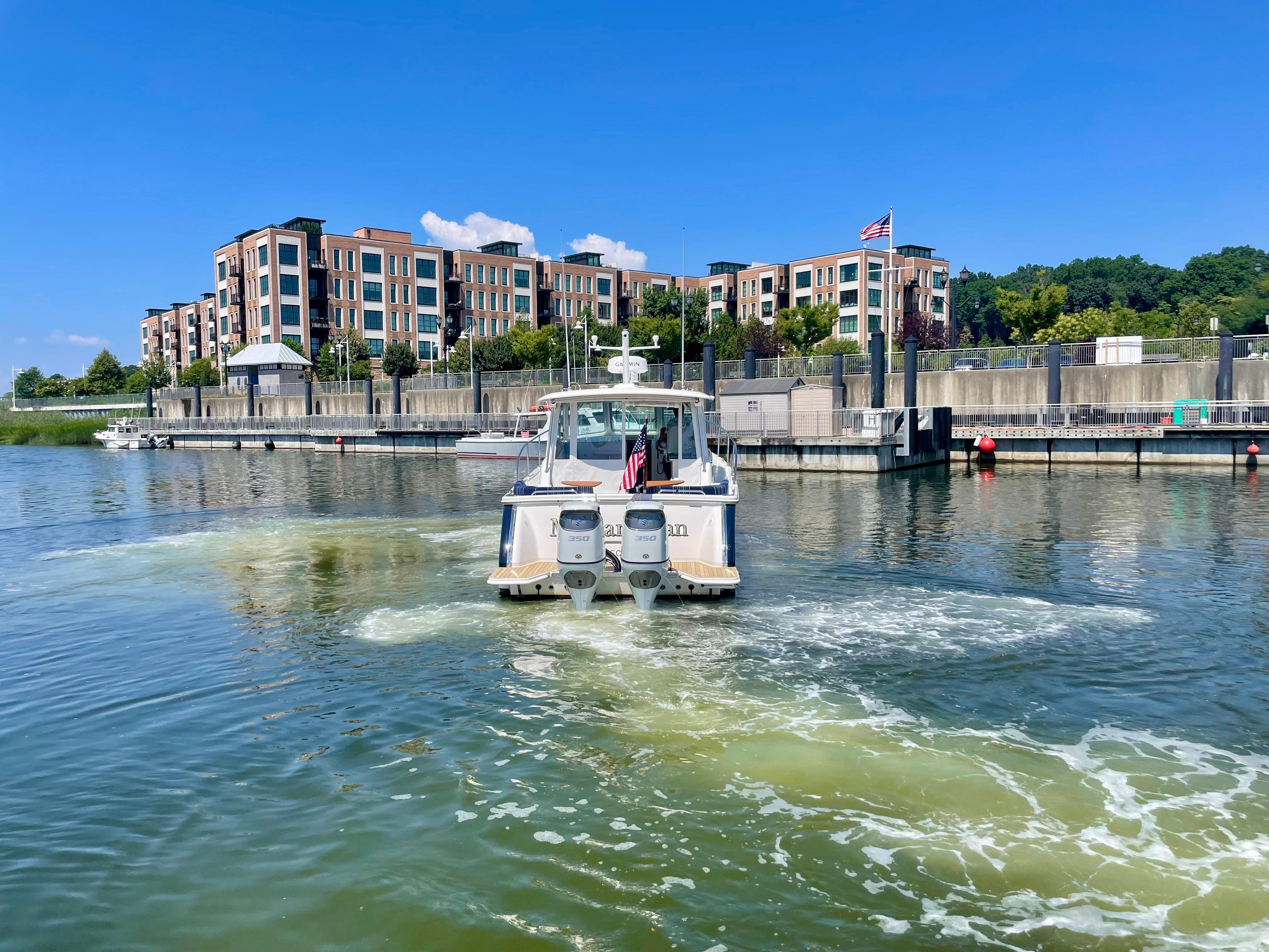 2023 Back Cove 34O boat cruising in a marina with modern buildings in the background.