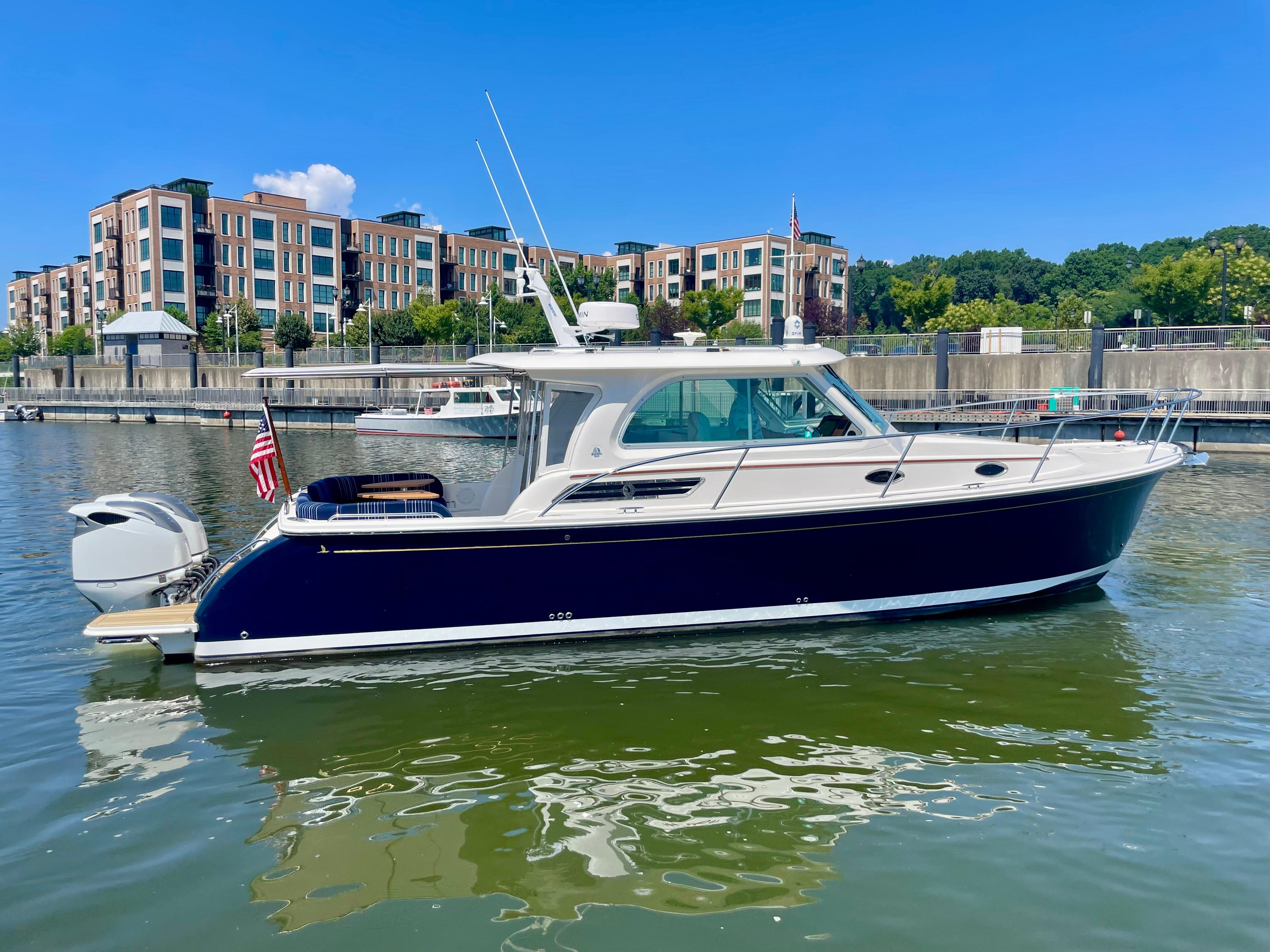 2023 Back Cove 34O boat docked in marina, modern buildings in background.