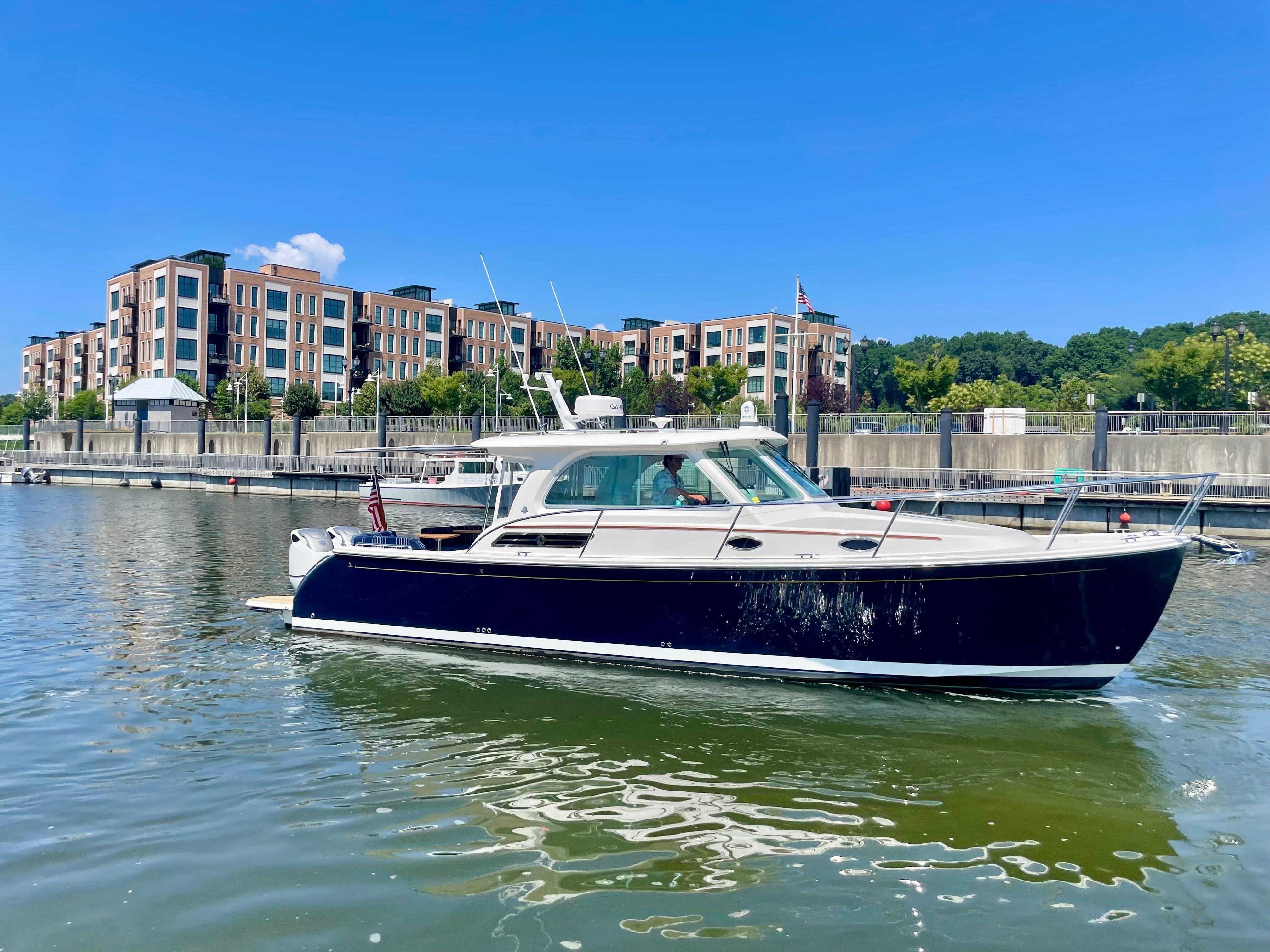 2023 Back Cove 34O boat docked in a marina with modern buildings in the background.