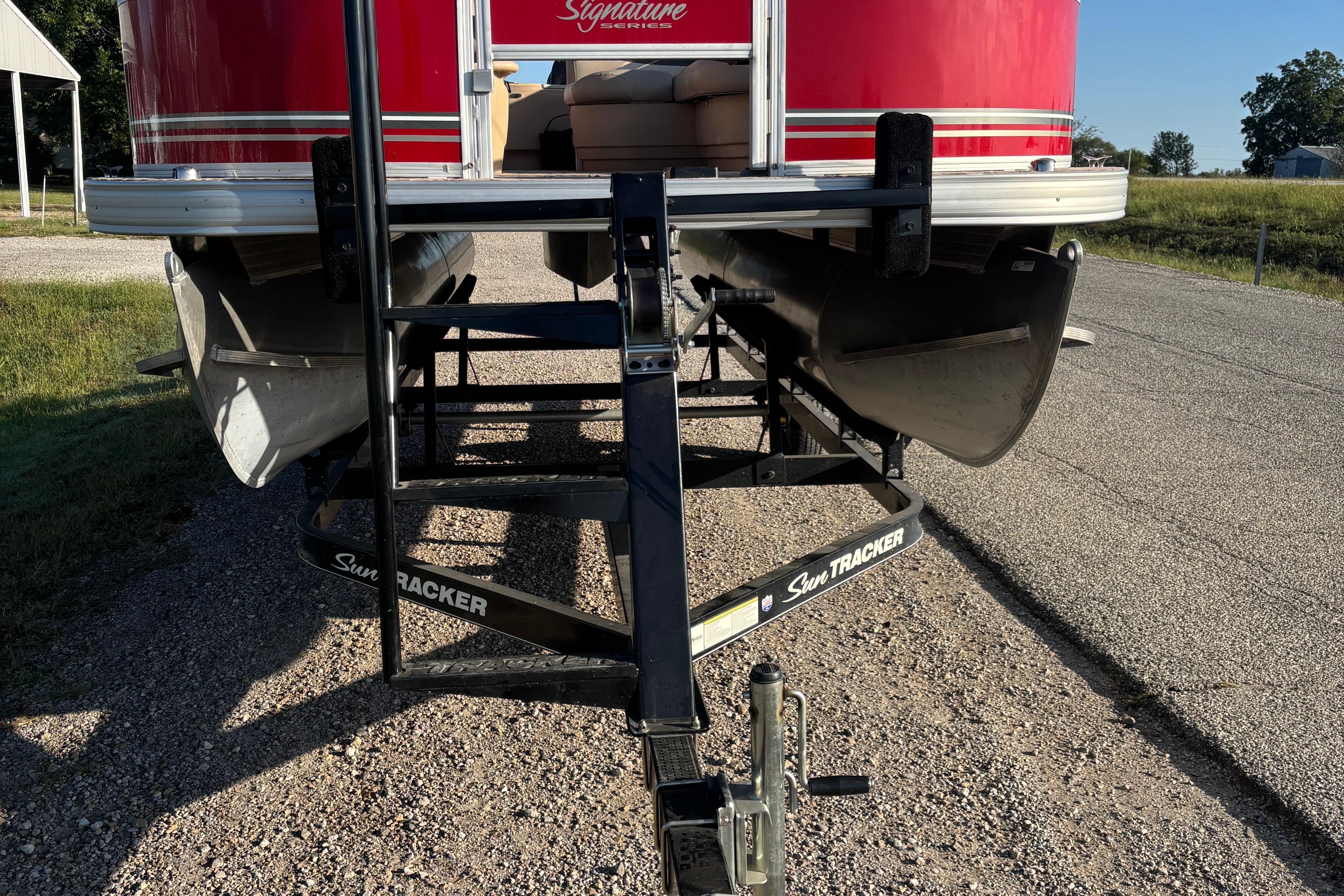 2014 Sun Tracker Bass Buggy 18 DLX pontoon boat on trailer, parked on gravel road.