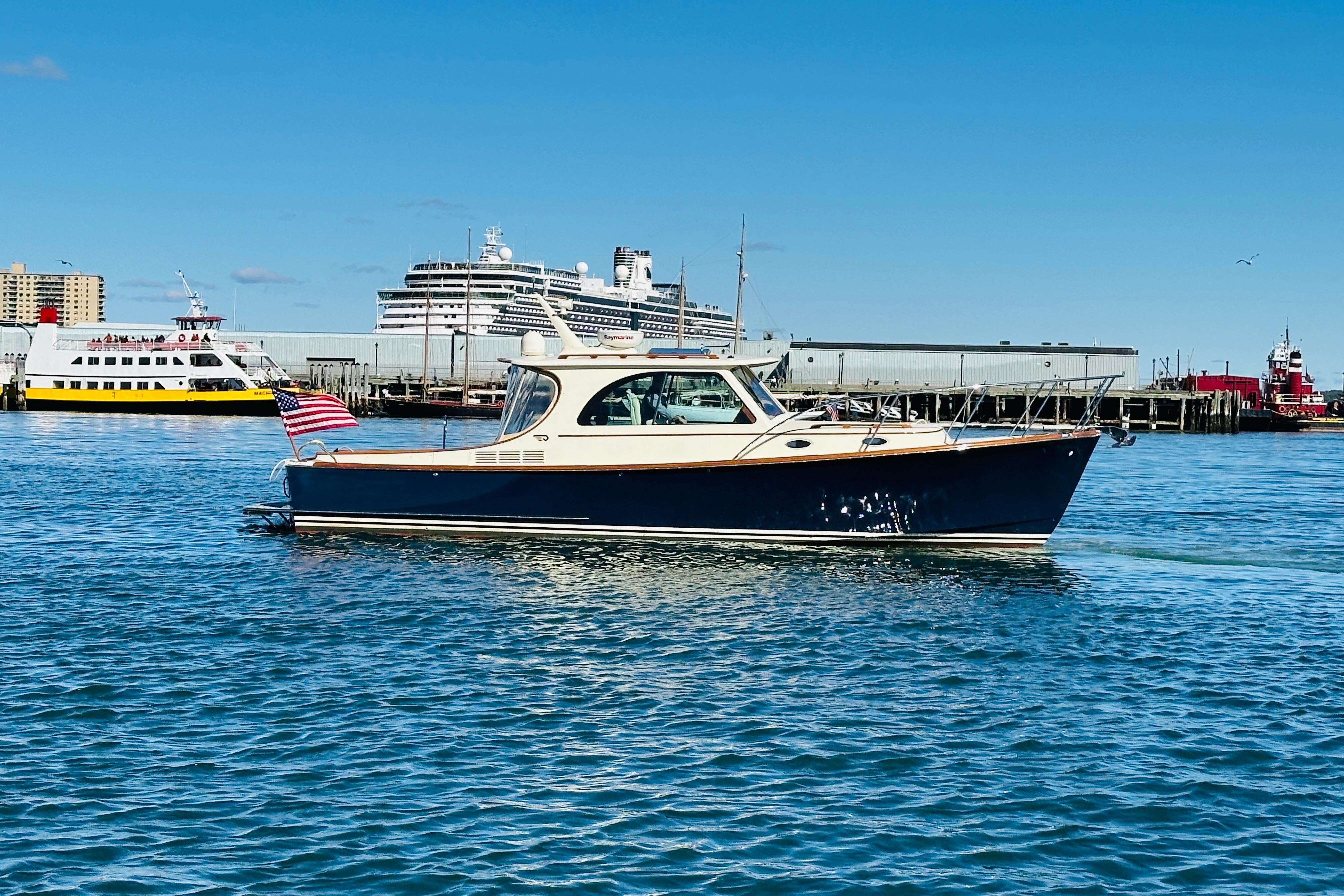 2012 Hinckley Picnic Boat MKIII cruising in a busy harbor with ships in the background.