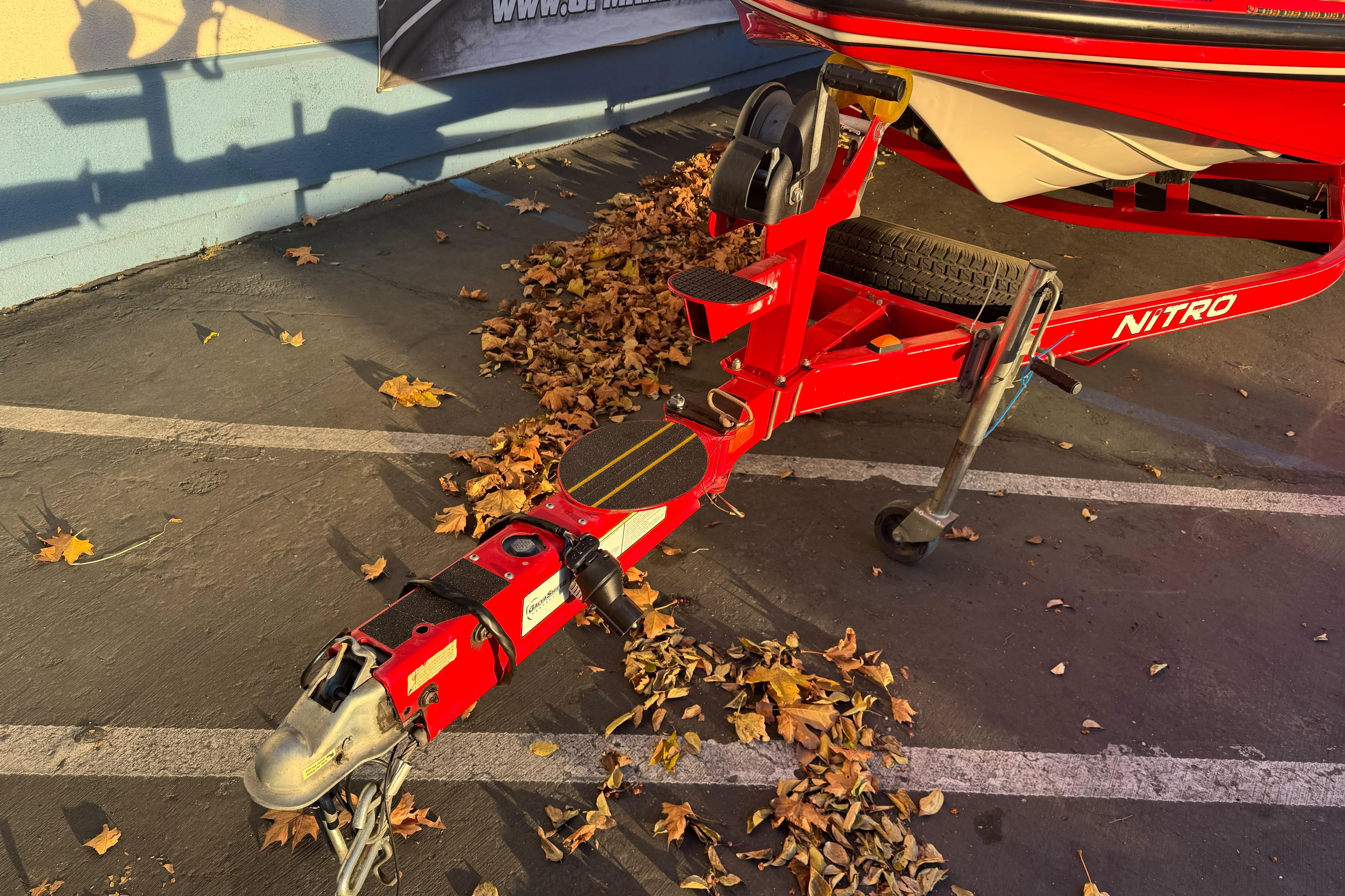 Red 2011 Nitro Z-9 DC boat trailer parked on asphalt with autumn leaves.