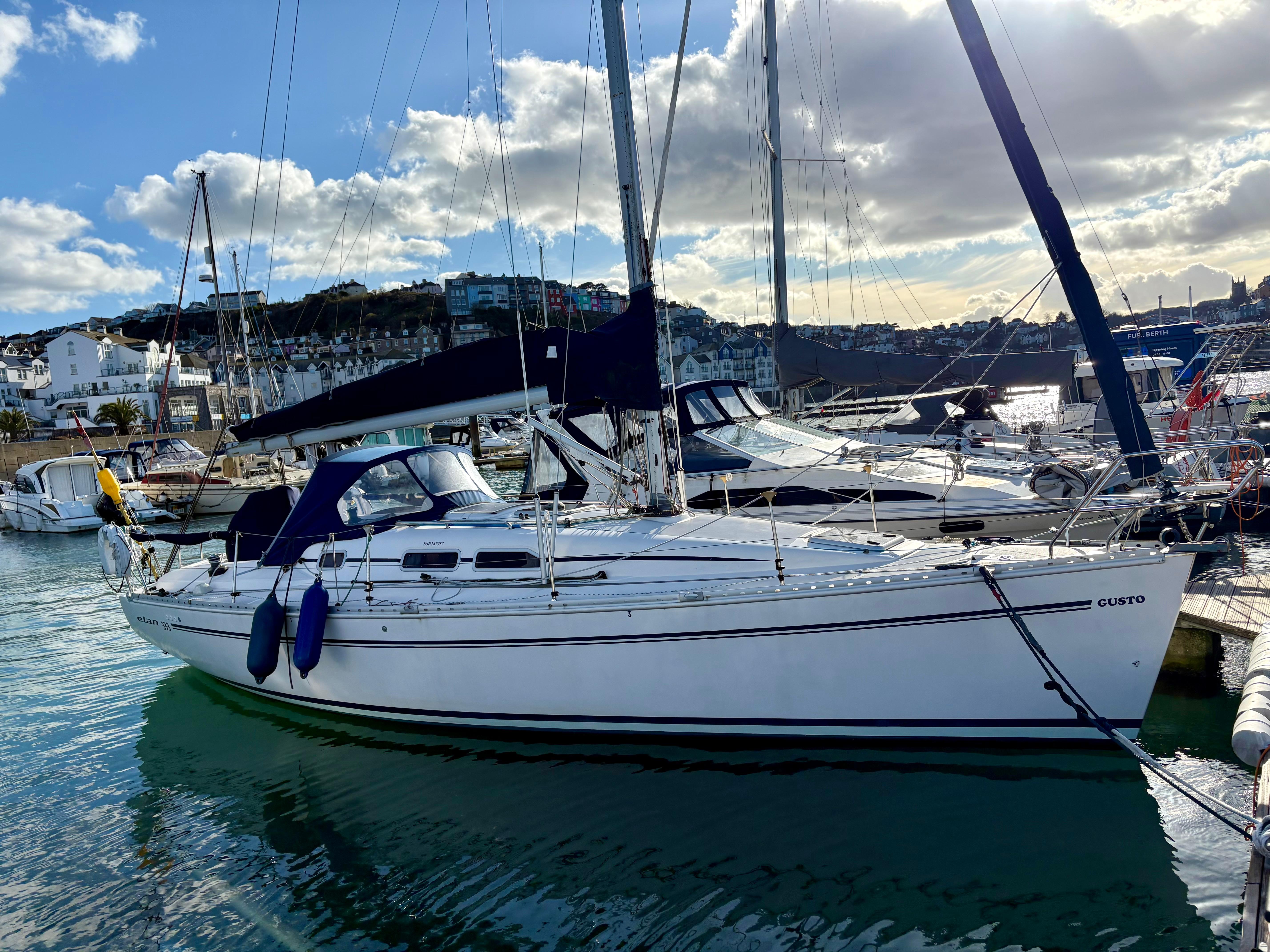 2004 Elan 333 sailboat docked in a sunny marina, surrounded by other boats.
