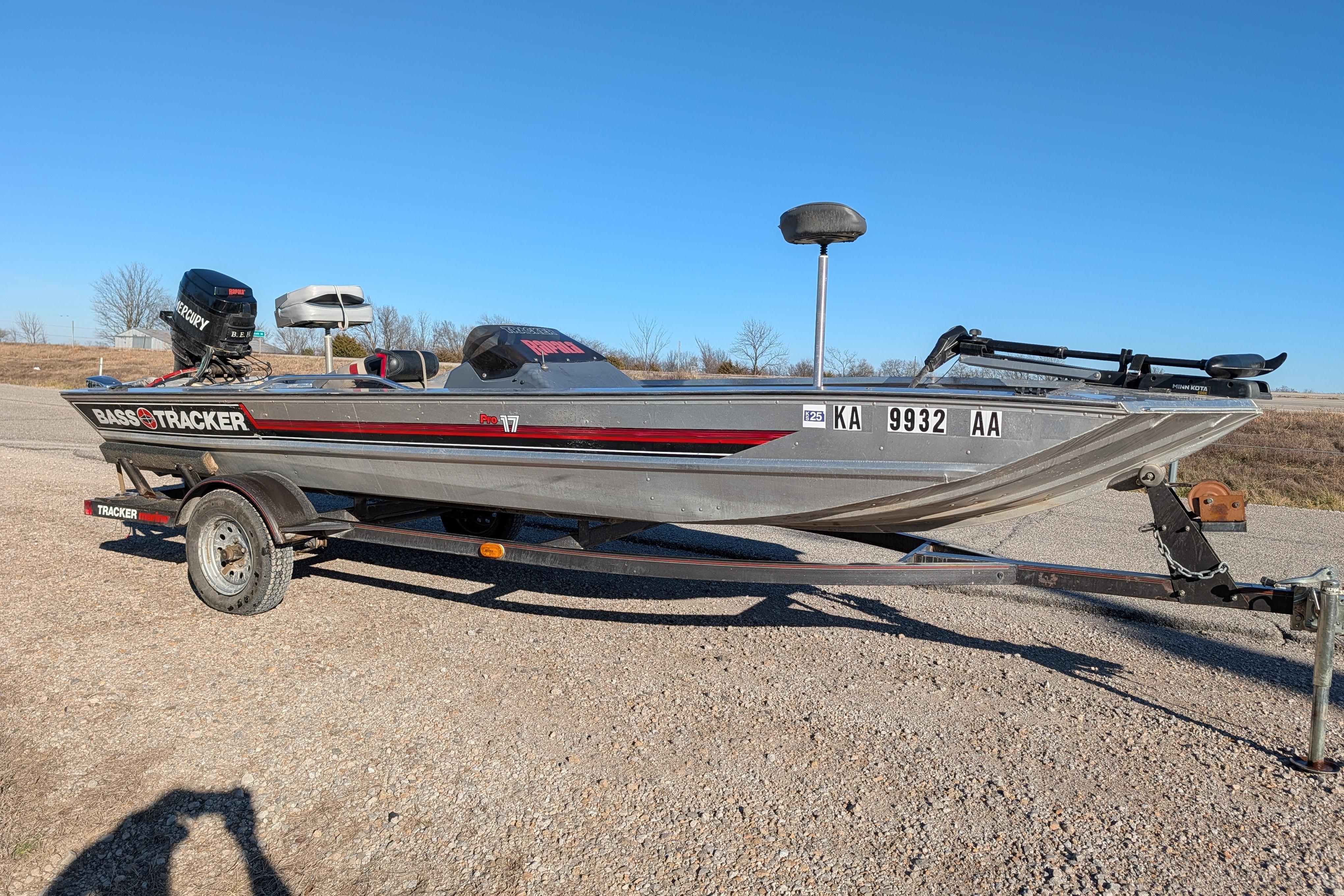 1988 Bass Tracker Pro 17 boat on trailer, parked on gravel, clear blue sky background.