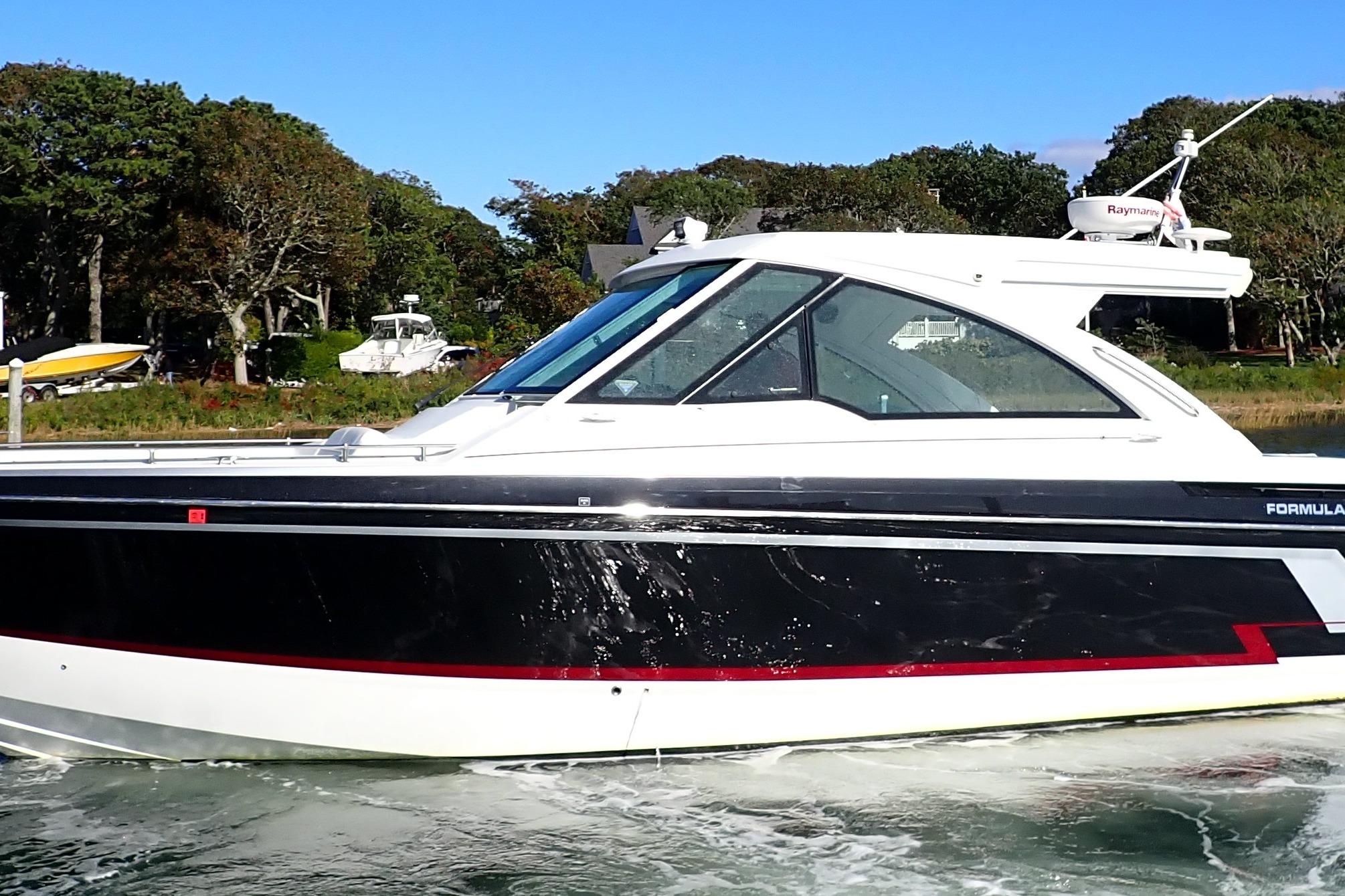 2022 Formula 380 Super Sport Crossover OB cruising on a sunny day near a wooded shoreline.