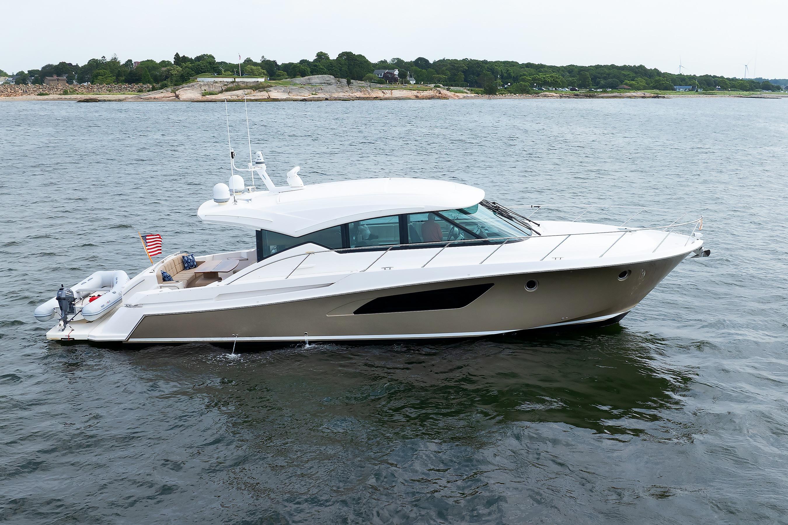 2014 Tiara 5000 Coupe yacht cruising on calm waters near a rocky shoreline.