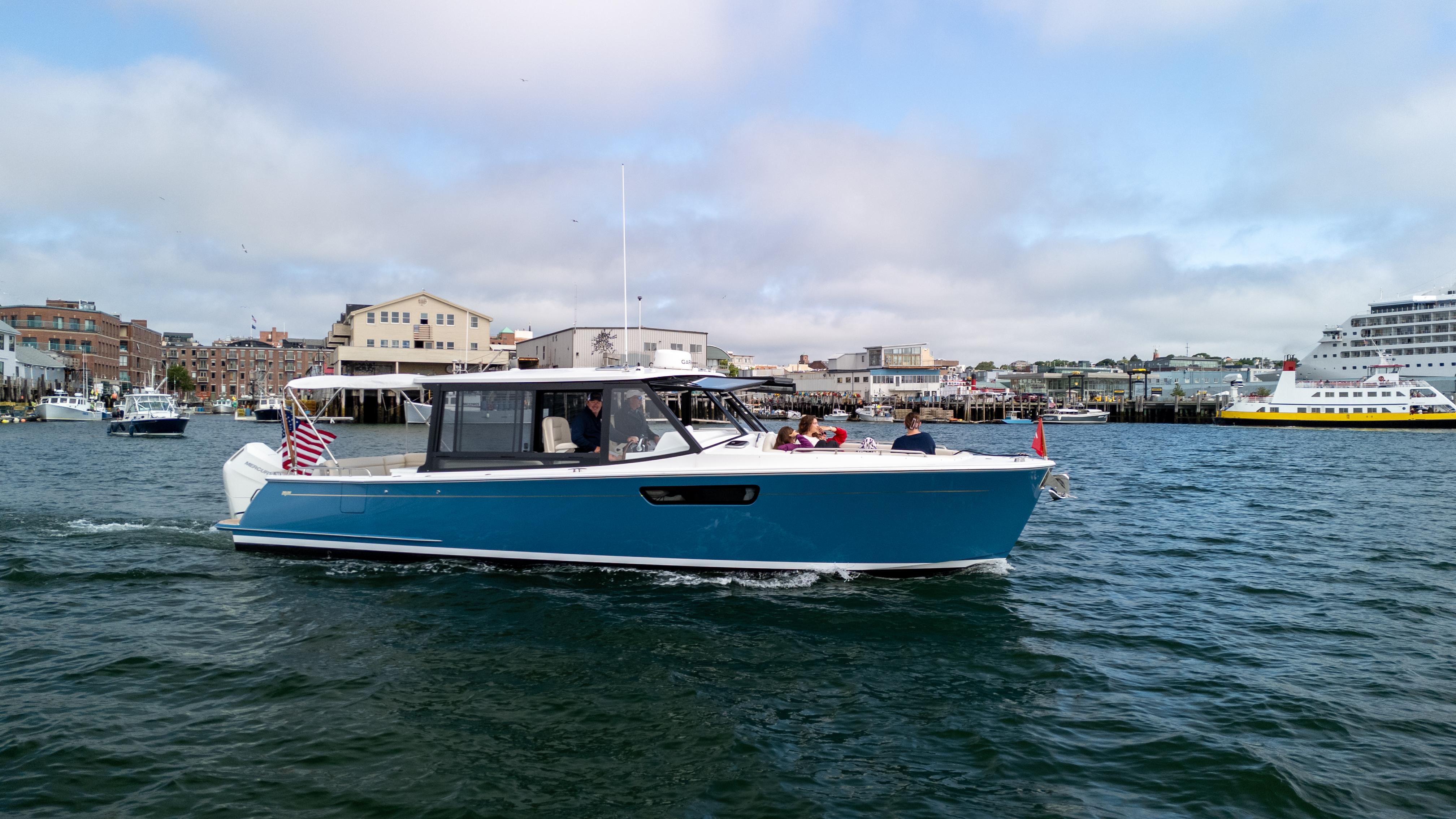 2025 MJM 3 boat cruising in a harbor with cityscape background.