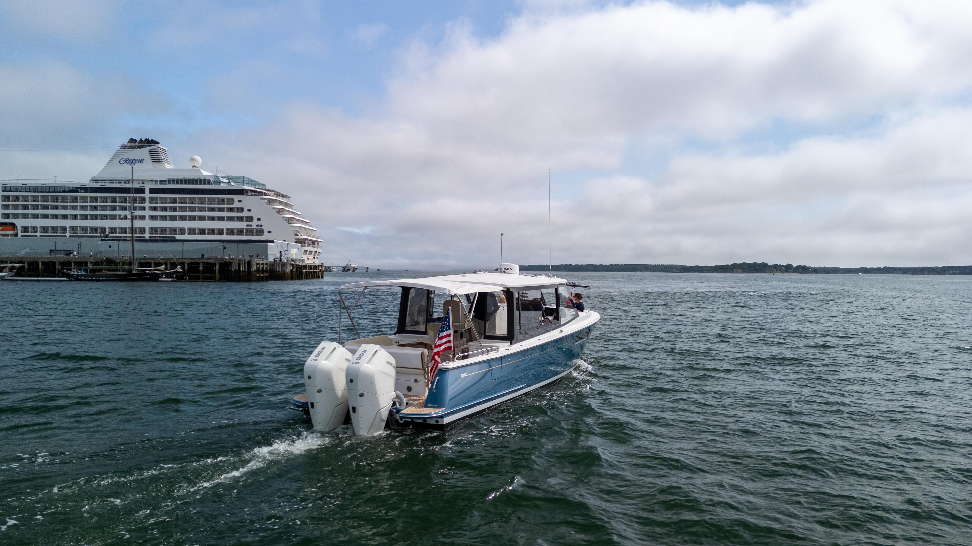 2025 MJM 3 boat cruising near a large cruise ship on a cloudy day.