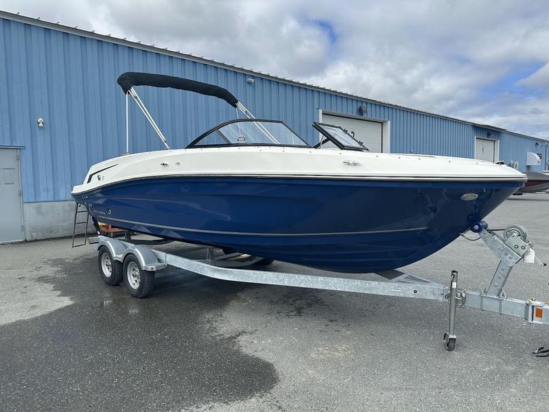 2023 Bayliner VR6 boat on trailer, blue hull, parked outside industrial building.