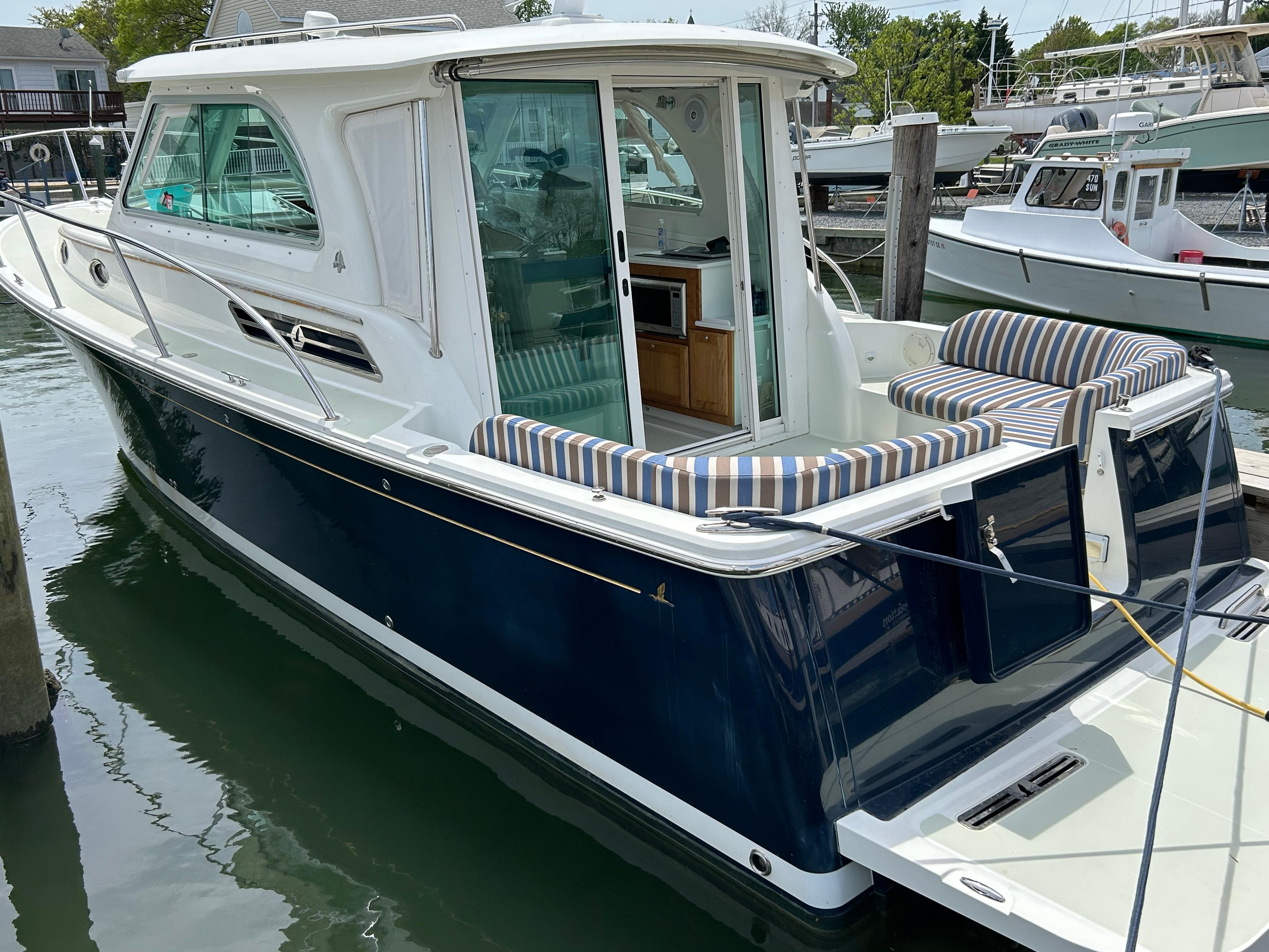 2018 Back Cove 32 boat docked, featuring a sleek navy hull and striped seating.