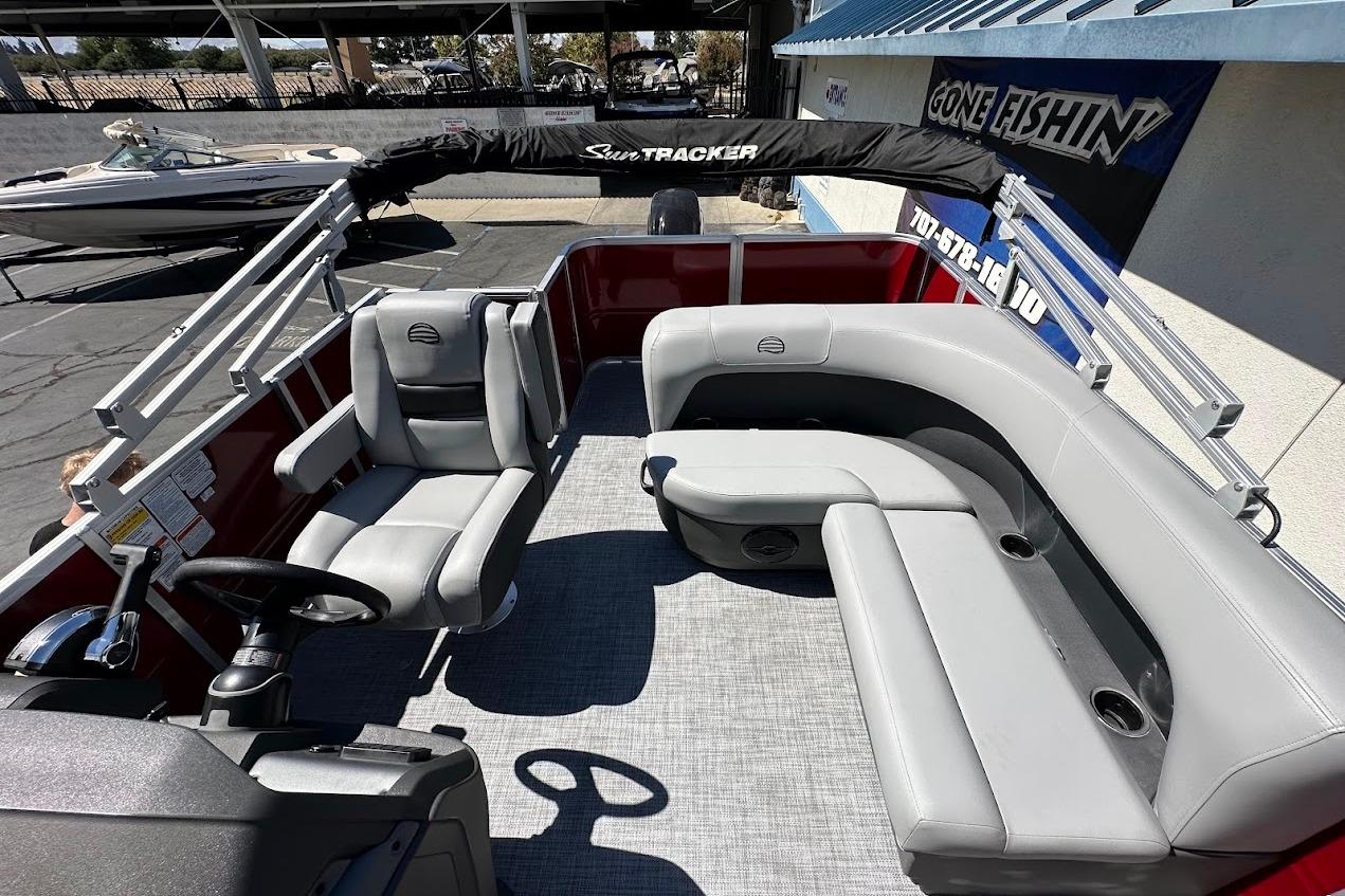 2026 Sun Tracker Party Barge 18 DLX with gray seating and steering wheel, docked outdoors.