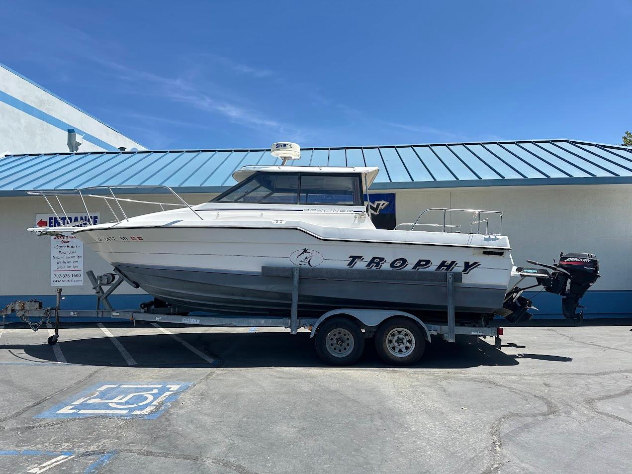 1992 Bayliner 2359 Trophy boat on trailer, parked outside a building under clear blue sky.