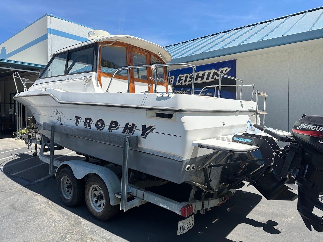 1992 Bayliner 2359 Trophy boat on trailer, parked outside a building under clear blue sky.