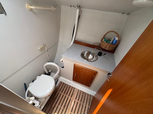 Compact bathroom in a 2000 Wyliecat 48 sailboat with toilet, sink, and wooden flooring.