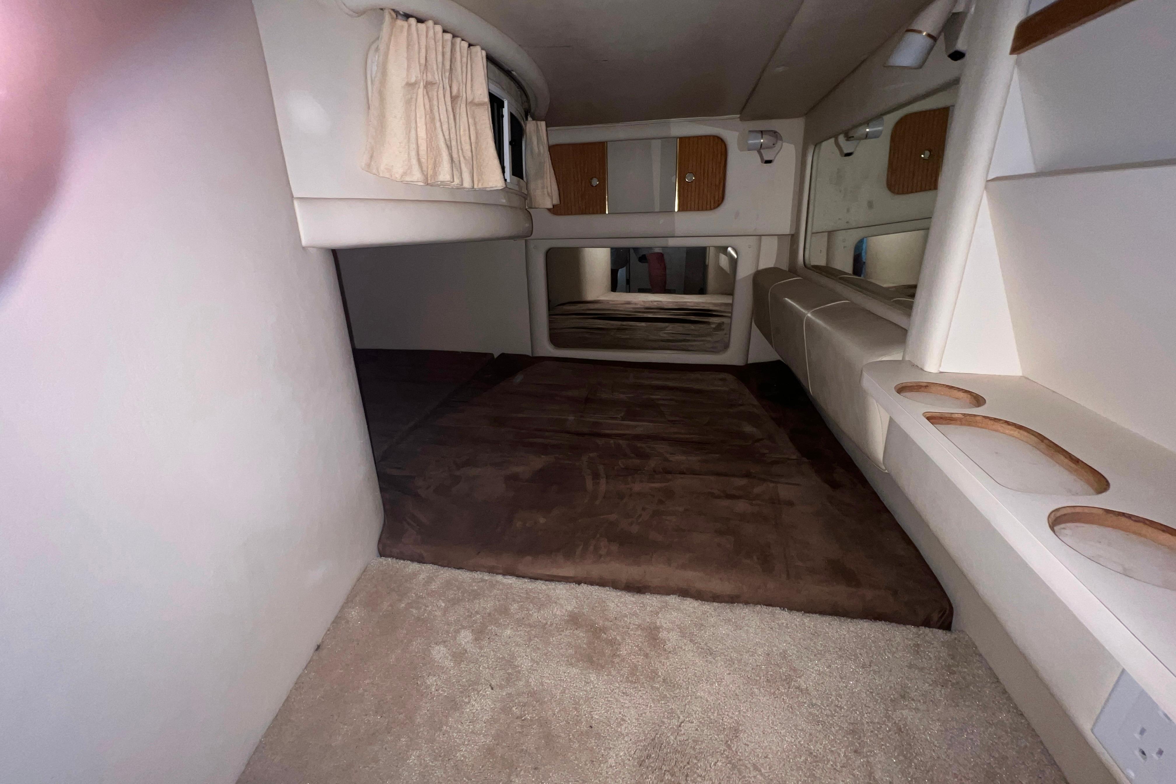 1999 Sea Ray 290 Sundancer cabin interior with bed, storage, and window curtains.